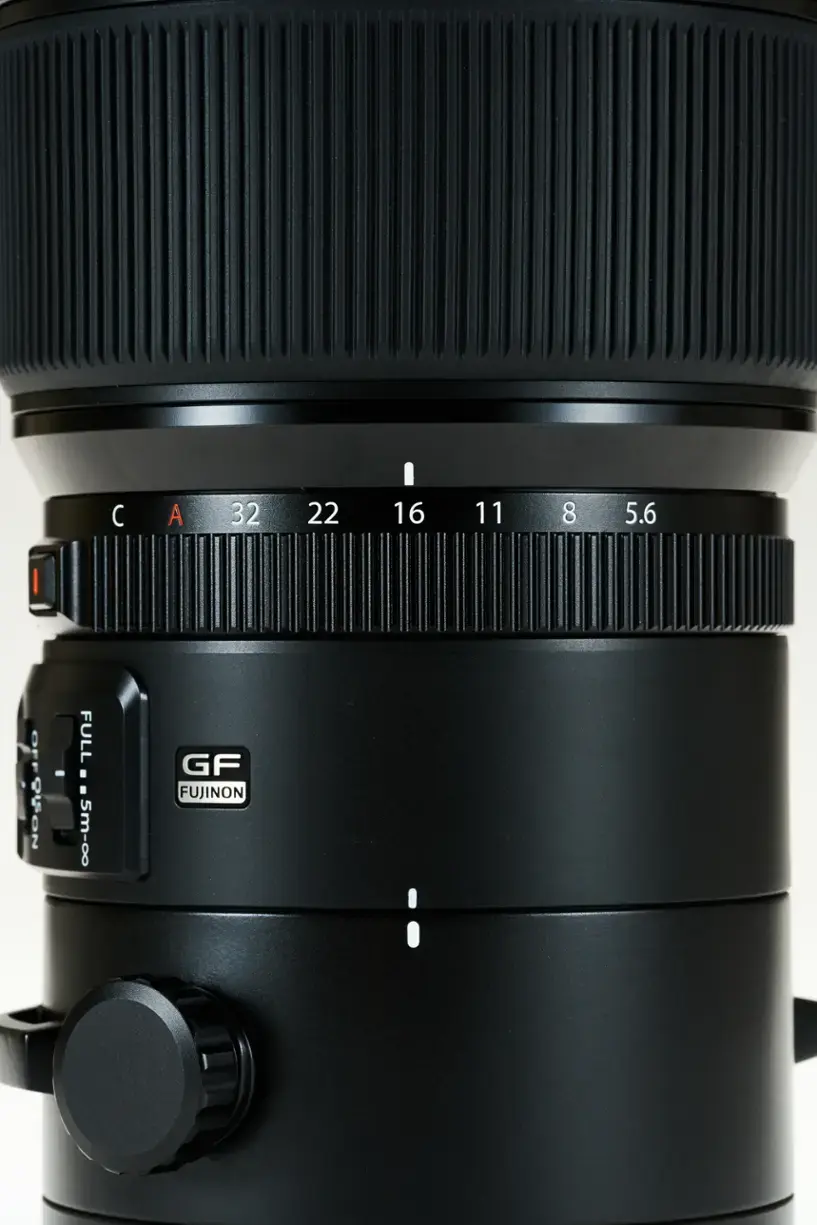The image features a large camera lens, which is likely a zoom lens. The lens is black and has a large aperture, making it suitable for capturing high-quality images. The lens is designed for use with a Fujifilm camera, as indicated by the brand name on the lens. The lens is positioned on a white background, which helps to emphasize its size and features.