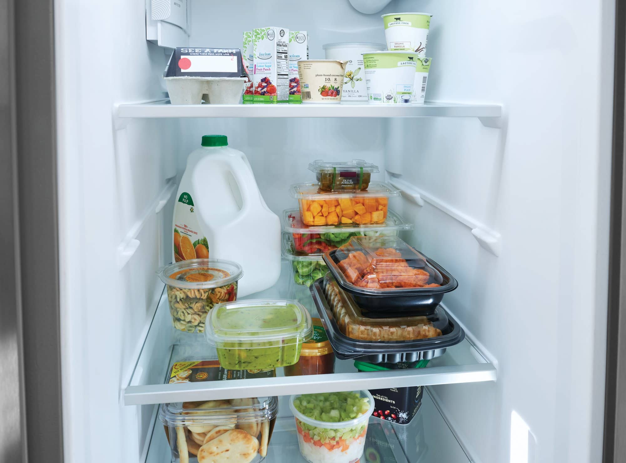 The refrigerator is full of food, including milk, juice, and various other items. There are several bottles, some of which are placed on the top shelf, while others are on the middle or bottom shelves. The refrigerator also contains a bowl and a cup. The variety of food items and containers suggests that the refrigerator is well-stocked and ready for use.