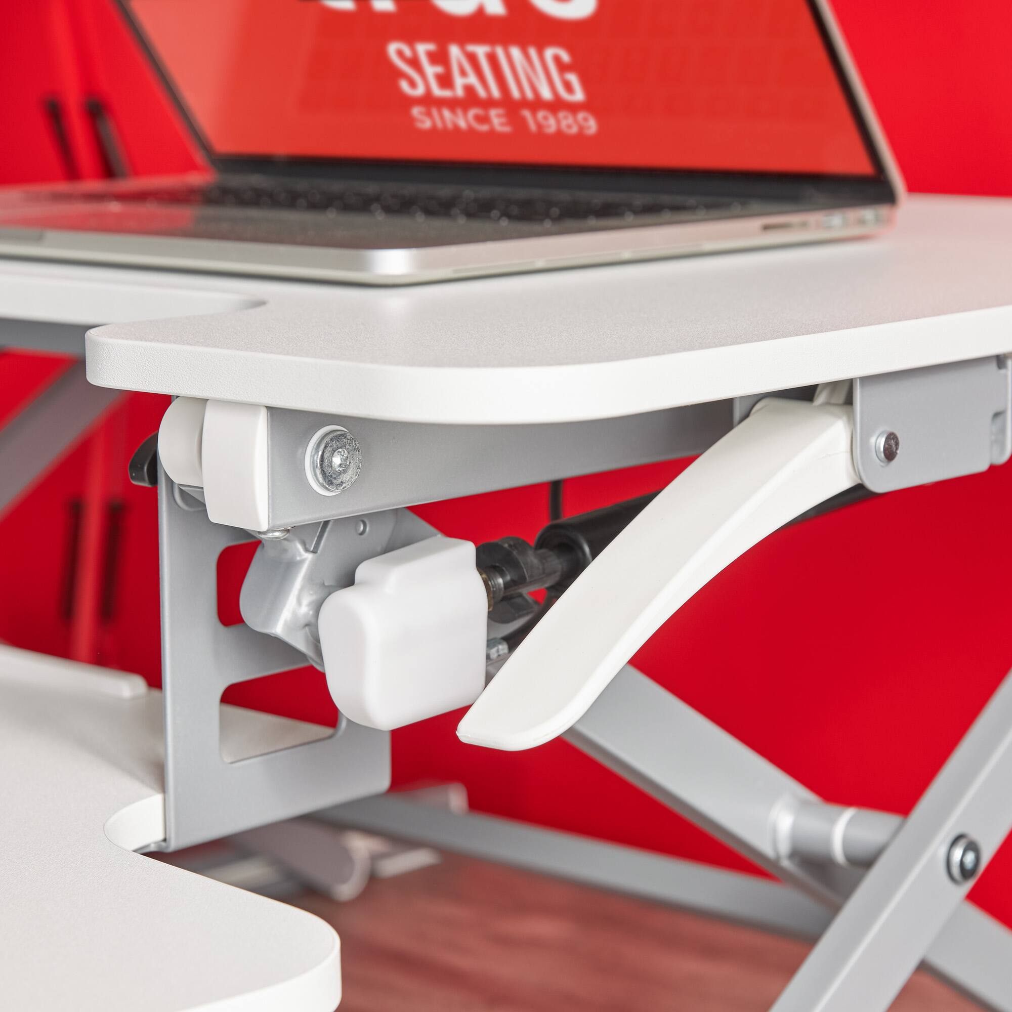 The image features a laptop computer sitting on a white table. The table has a stand attached to it, which is designed to elevate the laptop to a more ergonomic position for the user. The stand is white and has a black cord attached to it. The laptop is open and ready for use.