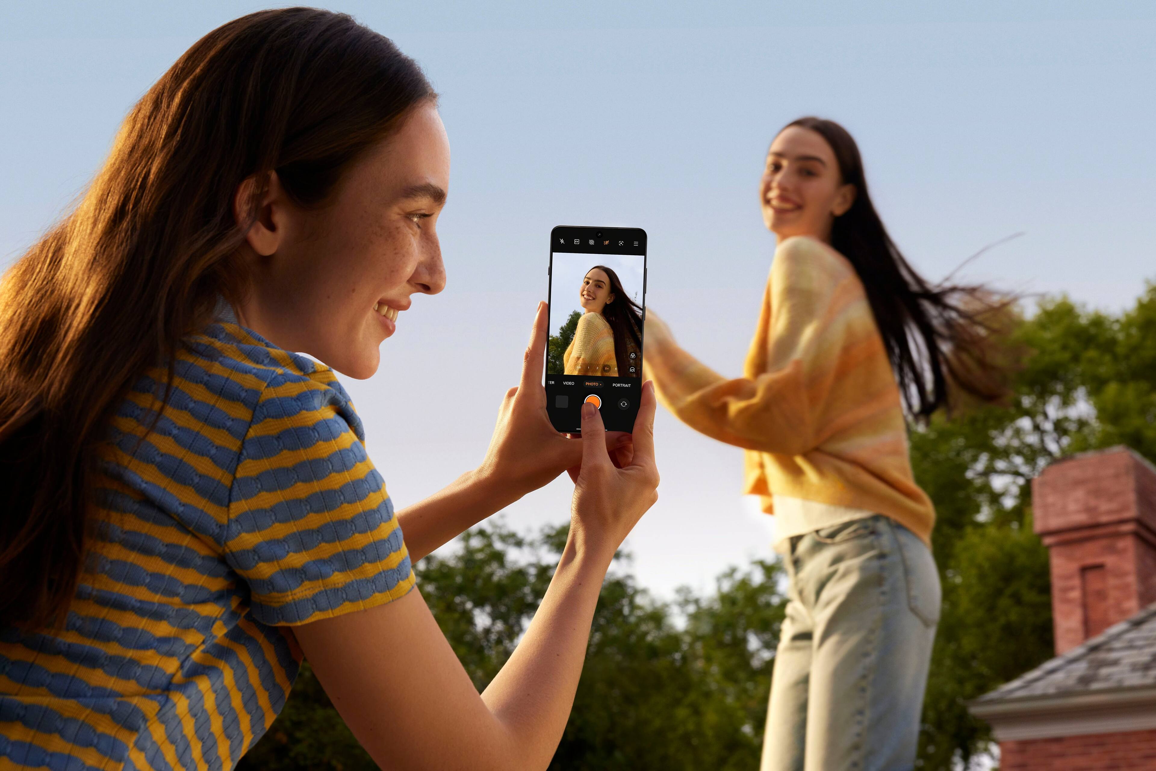 Two girls are taking a picture of each other using a cell phone.