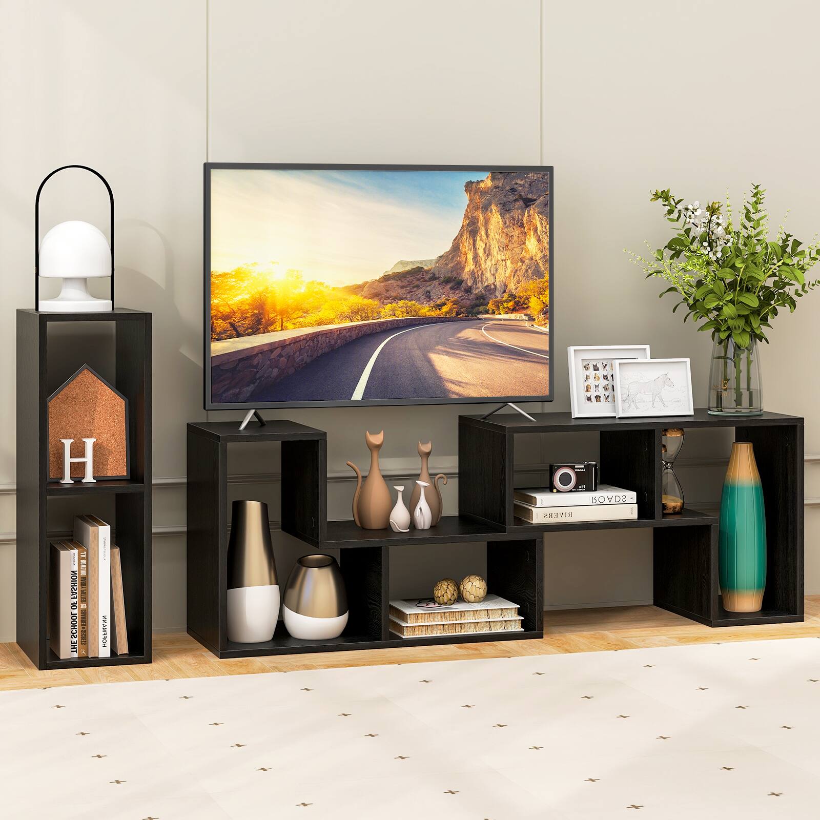 The image features a television sitting on a stand in front of a wall. The television is displaying a picture of a road, possibly a highway, with mountains in the background. The stand is filled with various items, including a vase, a potted plant, and several books. There are also two bottles placed on the stand. The overall scene creates a cozy and inviting atmosphere, perfect for relaxation or entertainment.