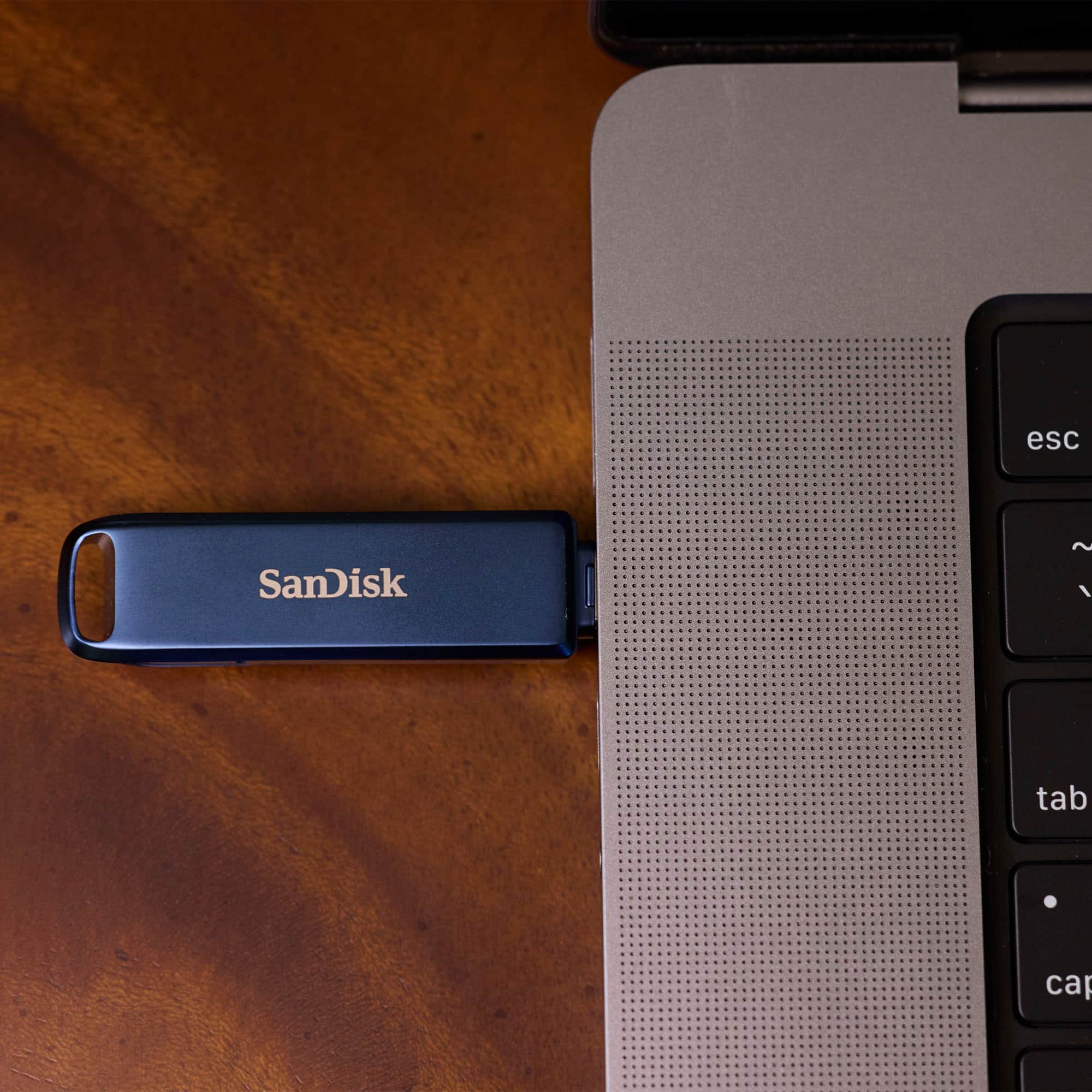 SanDisk is a brand of flash drives, memory cards, and other storage solutions. The image shows a SanDisk flash drive connected to a laptop. The flash drive is blue and is sitting on the laptop's keyboard.