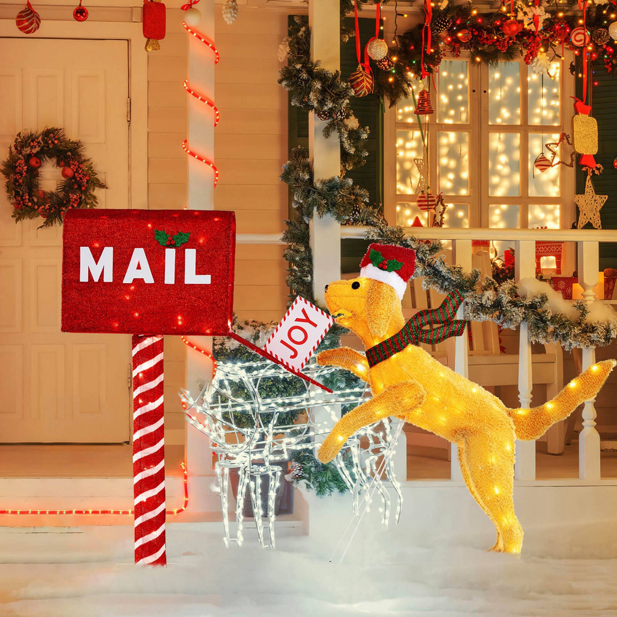 The image shows a festive scene with a mailbox and a dog-shaped decoration. The mailbox is red with the word "MAIL" on it, and the dog is wearing a Santa hat and scarf, holding a "JOY" sign. The scene is decorated with Christmas lights and ornaments.