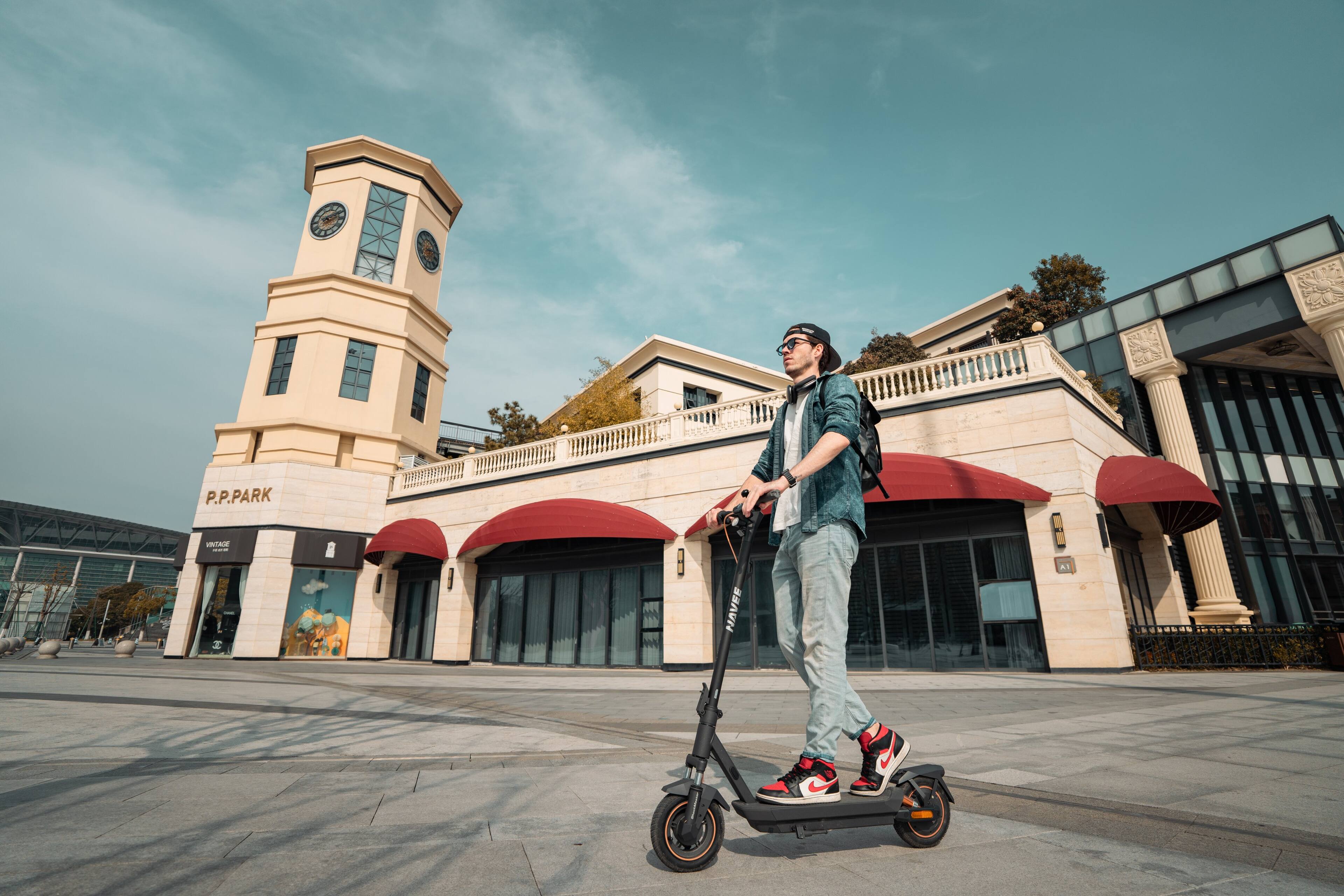 P.P. Park is a large building with a clock tower. A man is riding a scooter in front of the building.