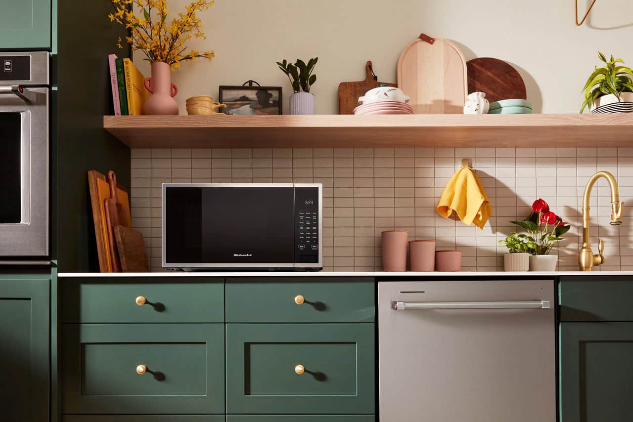 The text "B MOMOFU NOU 1 Esa . KitchenAid" is not relevant to the image. The image features a kitchen with a microwave, oven, and countertop. There are also potted plants and vases on the countertop.