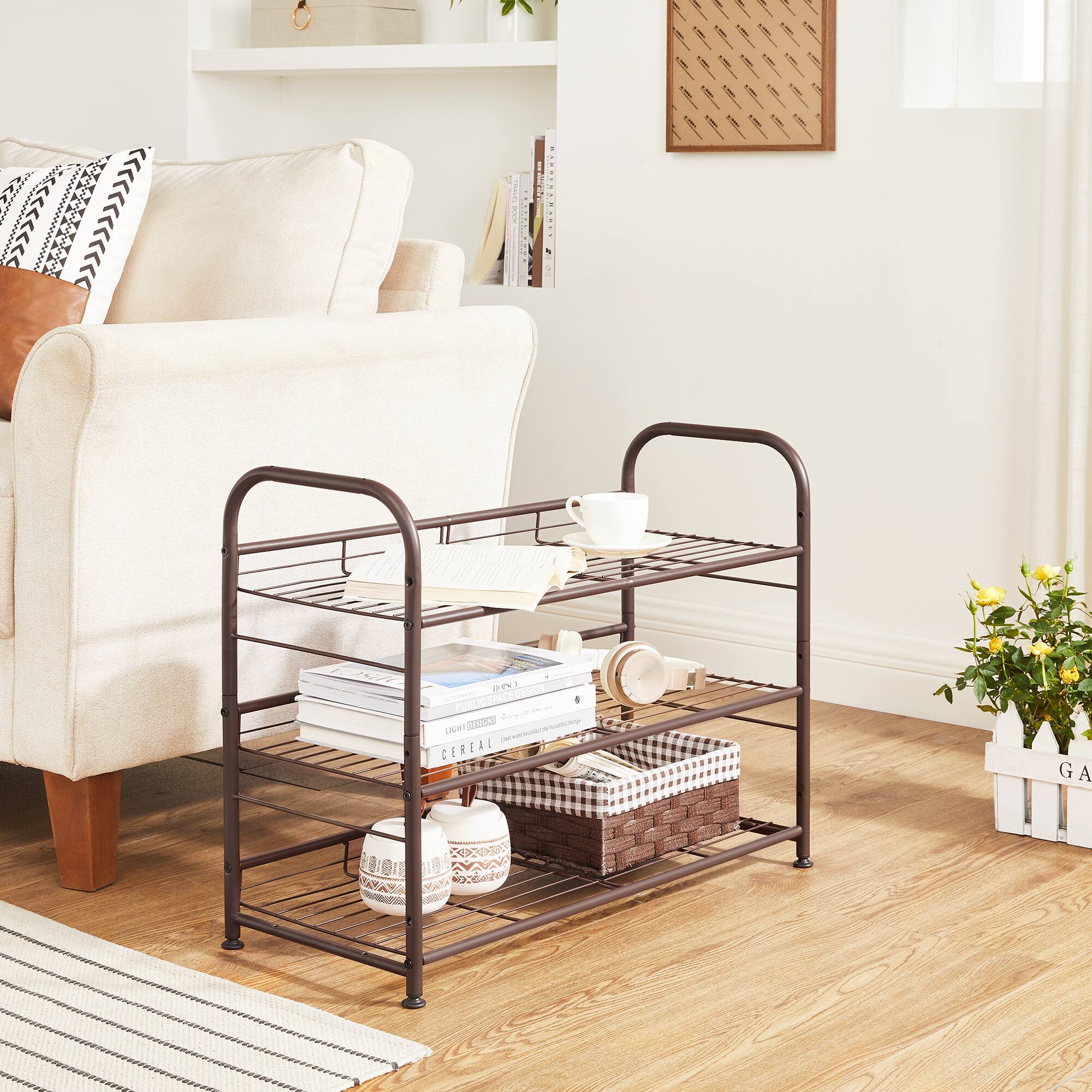 A public space designed for social interaction and relaxation, featuring a cozy seating area with a comfortable armchair, a metal side table holding a cup and saucer, and a bookshelf filled with books and decorative items. The space is accented with a woven basket, a ceramic container, and a potted plant labeled "GARDEN." The overall aesthetic is clean and inviting, with a focus on functionality and style.