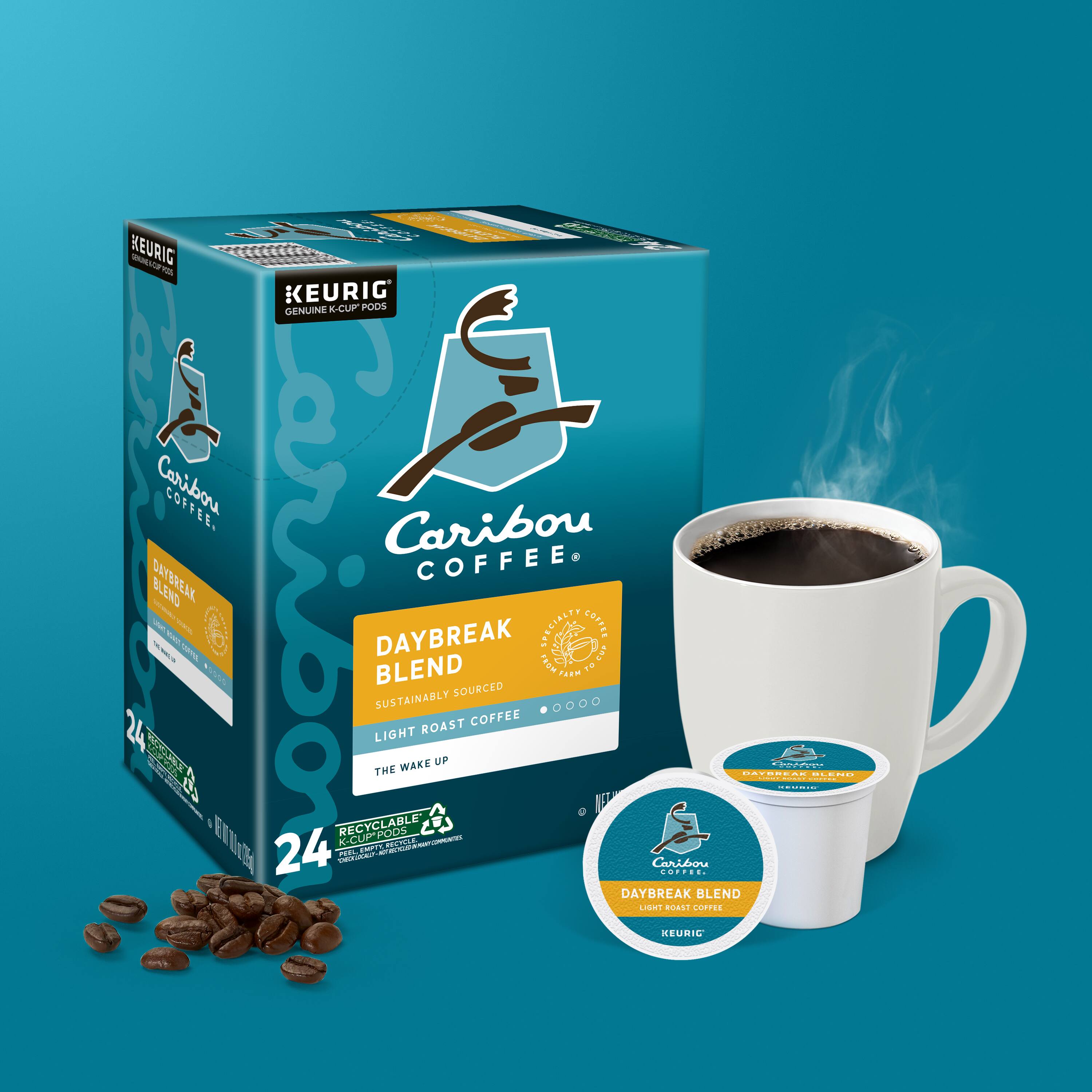 A box of Caribou Coffee Daybreak Blend is shown with a cup of coffee next to it. The box is blue and white, and the coffee is made from sustainably sourced and roasted coffee beans. The box contains 24 light and dark roasted coffee beans, and the cup is made from recyclable materials. The image showcases the brand's commitment to sustainability and quality coffee.