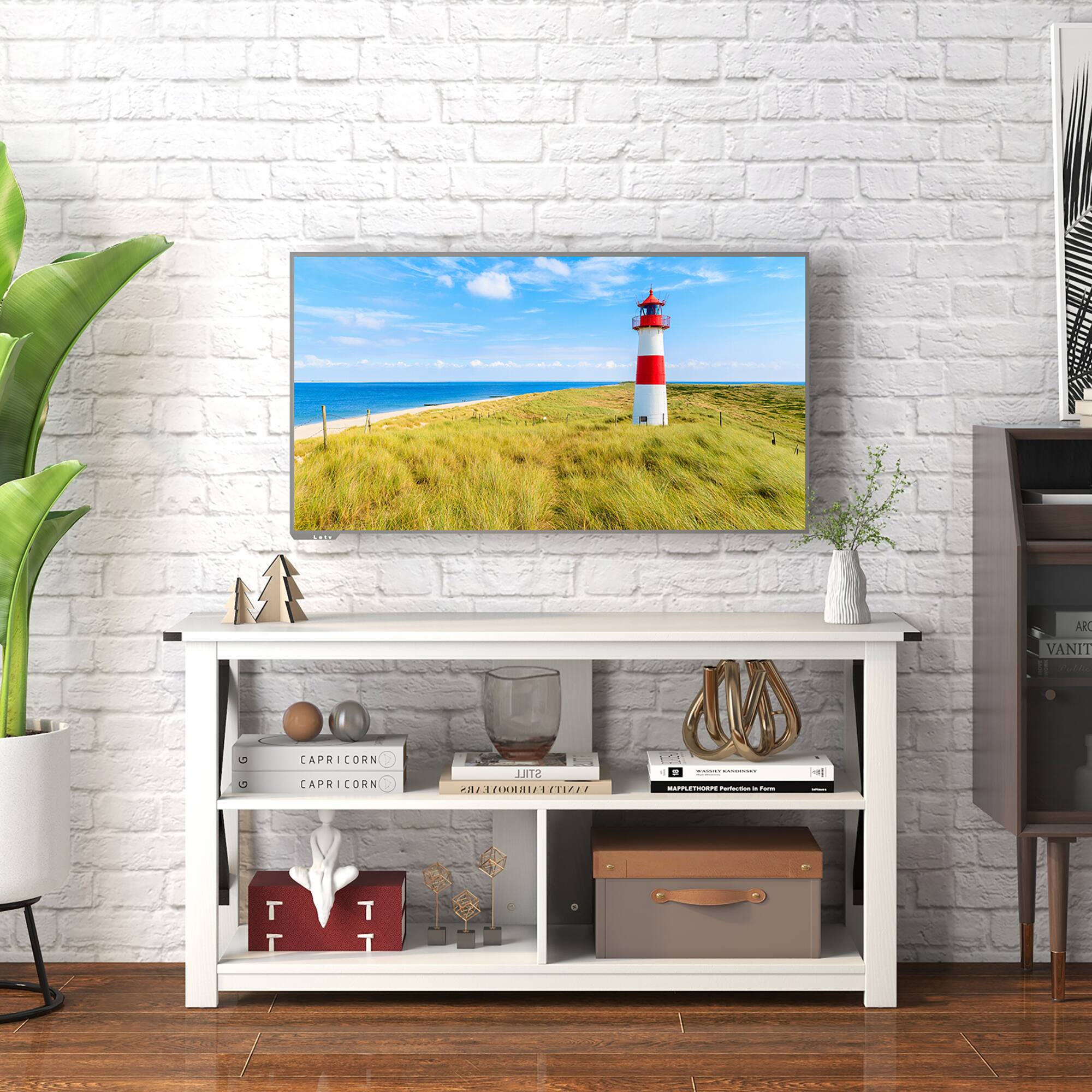 The image features a white desk with a television on it. The TV is displaying a picture of a lighthouse. The desk is surrounded by various items, including a potted plant, a vase, a book, and a clock. There is also a suitcase and a handbag placed nearby. The scene appears to be set in a living room or a similar space.
