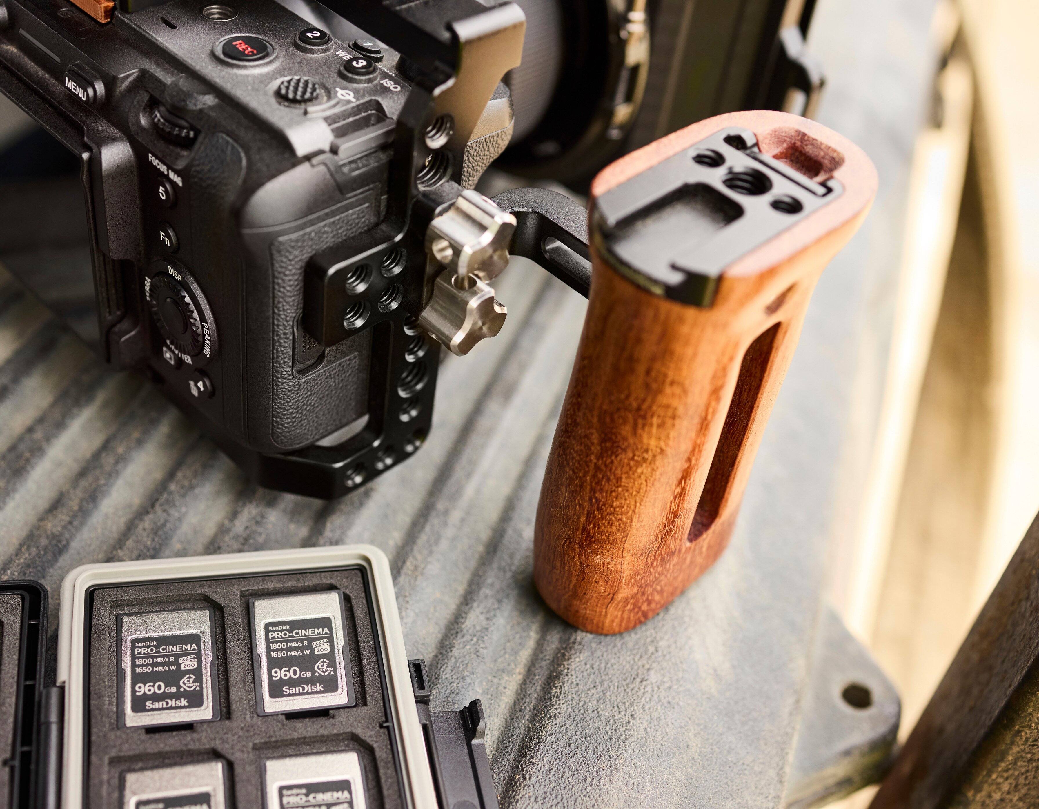 The image features a camera with a wooden case and a memory card holder. The memory card holder is designed for SanDisk memory cards, specifically for the SanDisk PRO-CINEMA series, which include the 1650, 1800, and 960 models. The camera is placed on a wooden table, and the memory card holder is positioned next to it. The focus of the image is on the camera and memory card holder, showcasing their compatibility and usefulness for photographers and videographers.