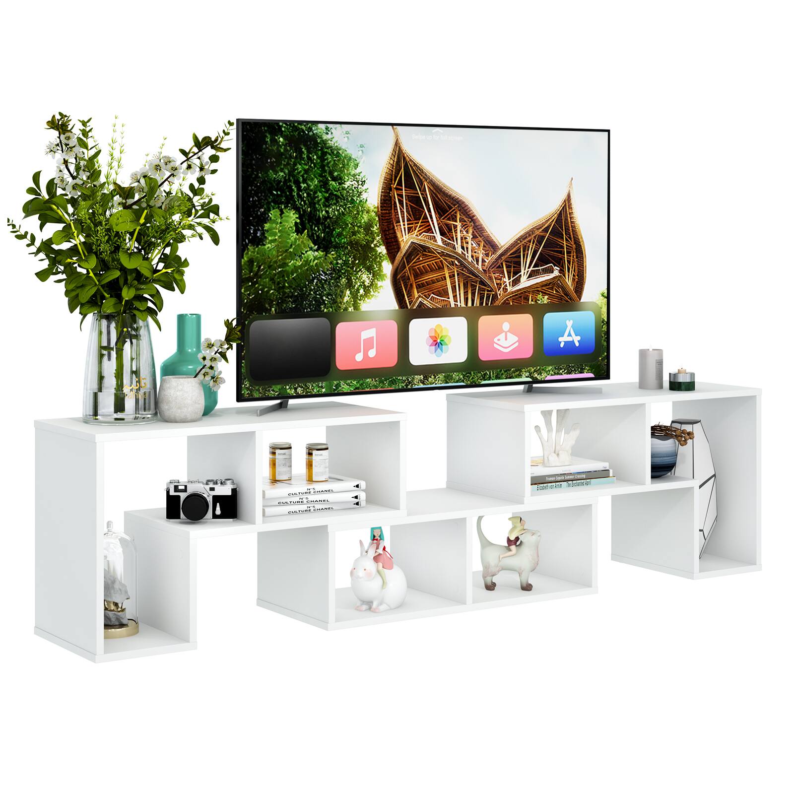 The image features a flat screen TV placed on a stand, surrounded by various items. There are two vases, one on the left side and the other on the right side of the TV. Additionally, there are two books, one on the left and the other on the right side of the TV. A potted plant is located on the left side of the TV, and a remote control can be seen on the right side. The scene also includes a cat figurine on the right side of the TV, and a bottle is placed on the left side.