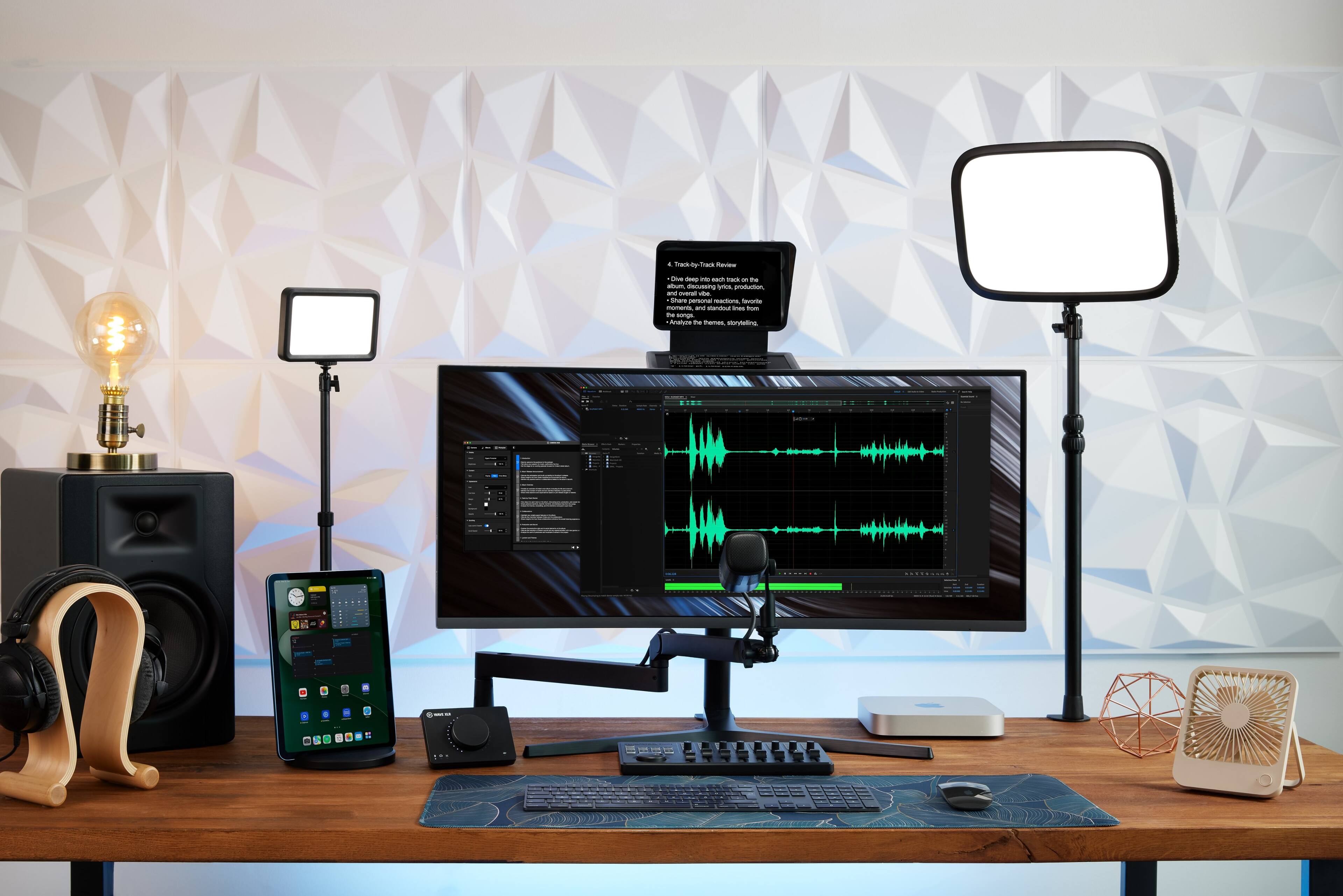 The image features a wooden desk with a computer setup, including a keyboard and a monitor. There is also a cell phone on the desk. The desk is located in front of a wall with a patterned design. The desk is equipped with two lights, one on each side, and a microphone. The scene appears to be a workspace for someone who is likely involved in video editing or multimedia production, as suggested by the presence of the microphone and the computer setup.