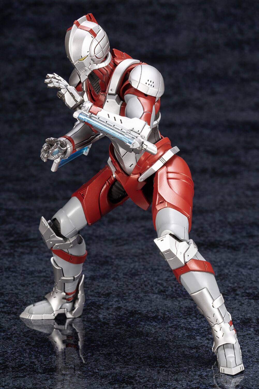 The image shows a detailed action figure of a character in a red and white armored suit, holding a futuristic weapon. The figure is posed dynamically, with one leg forward and the other back, as if ready for action. The armor is sleek and high-tech, featuring intricate designs and a helmet with a visor. The background is a dark, textured surface that contrasts with the figure, highlighting its details.