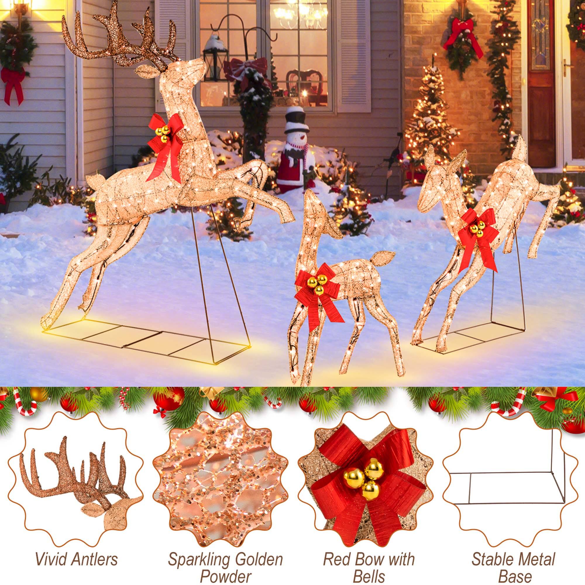 The image features a group of deer figurines with red bows on their heads, standing in the snow. The deer are placed on a stable metal base, and they are surrounded by various Christmas decorations, such as a Santa Claus figure and a Christmas tree. The scene is set in a snowy yard, creating a festive and holiday atmosphere.