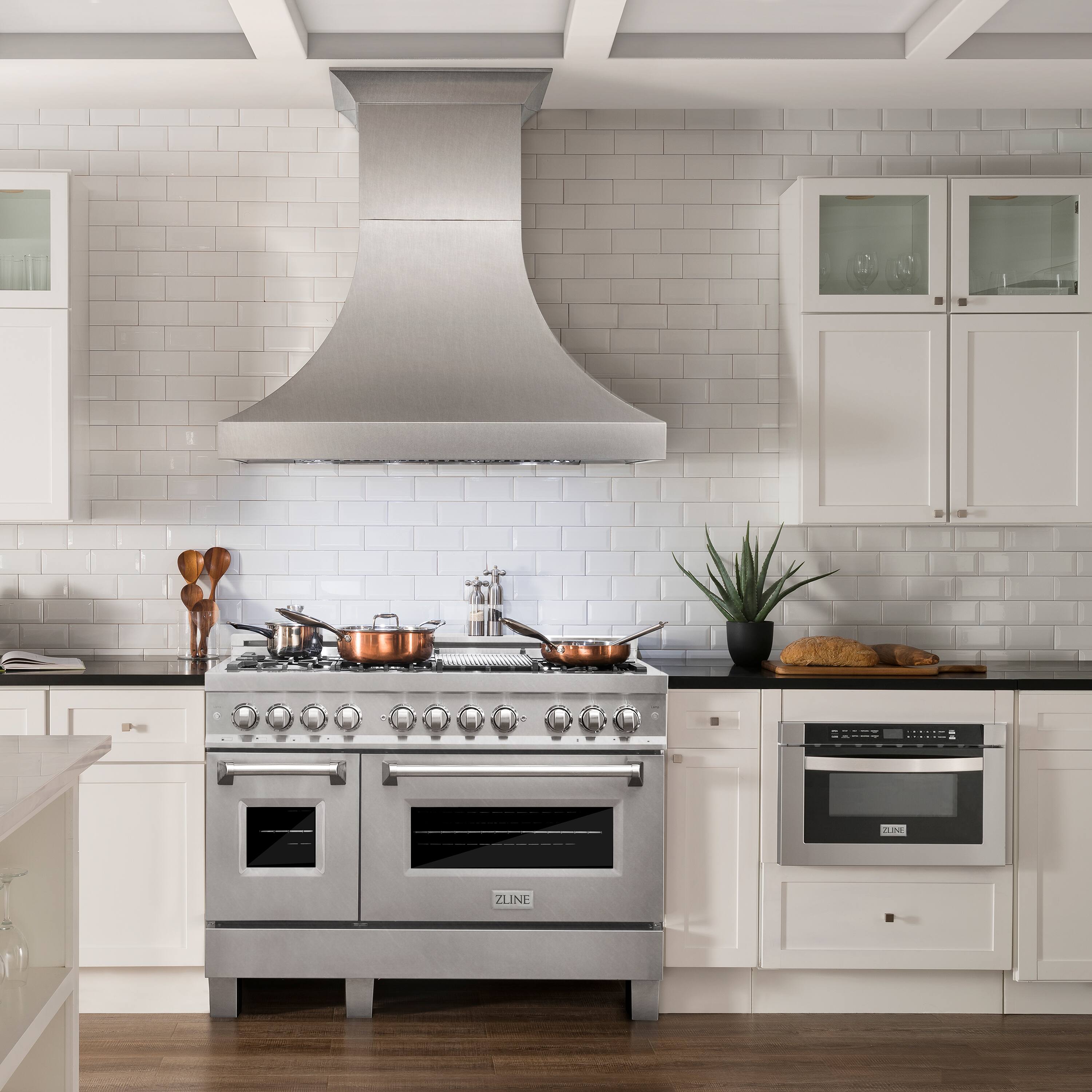 The image shows a kitchen with a stainless steel stove top oven and a hood. The oven has a stainless steel finish and is positioned under a ventilation fan. The kitchen also features white cabinets and a countertop. Additionally, there is a potted plant in the kitchen, adding a touch of greenery to the space.