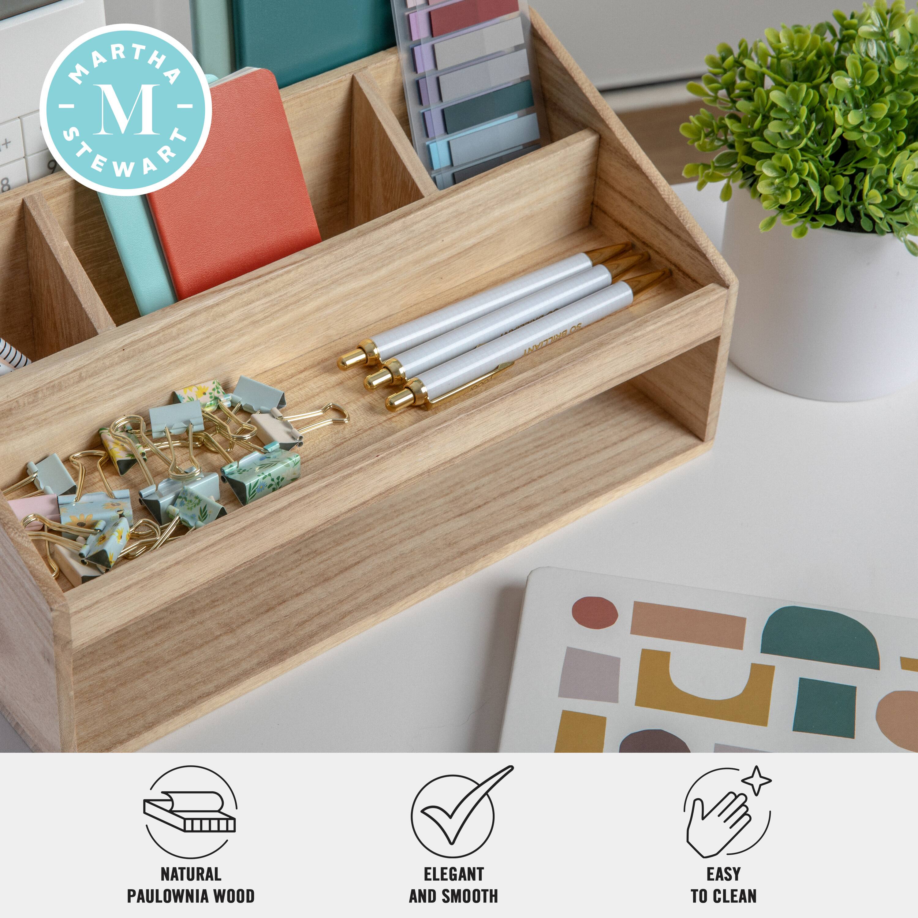 The image features a wooden box with a drawer that contains various items such as pens, pencils, and books. The box is placed on a table, and there is a potted plant nearby. The text on the image reads "Martha Stewart Natural Paulownia Wood Elegant and Smooth Easy to Clean."