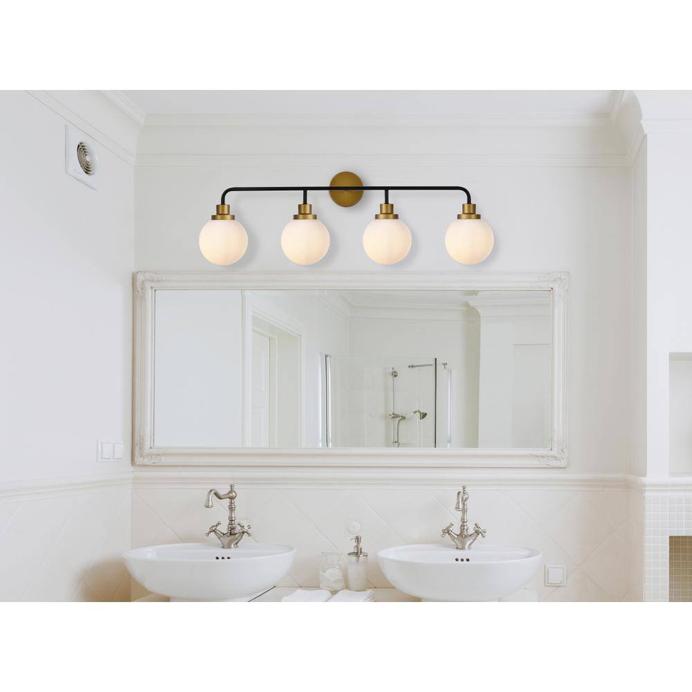 The image shows a modern bathroom with a clean, minimalist design. The room features a large mirror with a decorative frame, flanked by two white vessel sinks with elegant silver faucets. Above the mirror, there is a stylish light fixture with four round bulbs. The walls are painted white, and the lower part of the wall is tiled with white subway tiles. The overall aesthetic is bright and airy, with a focus on simplicity and elegance.