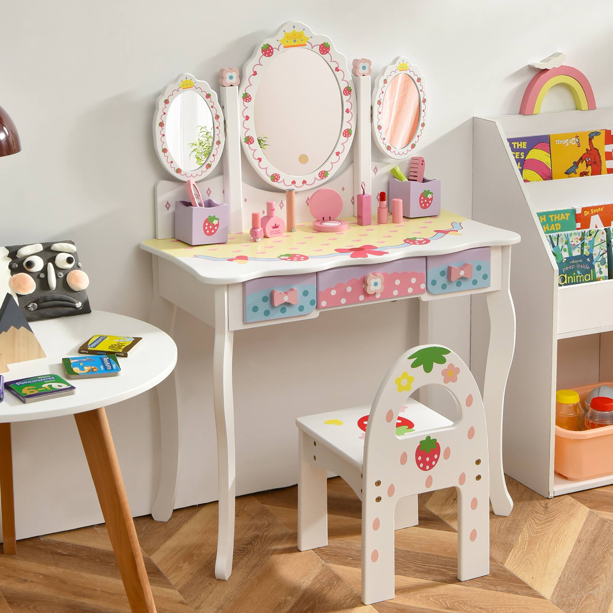 The desk is designed for children, featuring a playful and colorful theme with strawberry patterns. It includes a mirror, a small stool, and storage compartments.