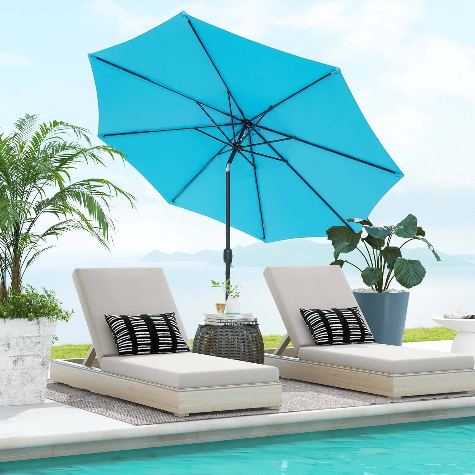 The image features a blue umbrella providing shade over a pair of lounge chairs. The chairs are positioned on a patio near a pool, with a potted plant and a vase nearby. The umbrella is open and covering the chairs, creating a comfortable and relaxing outdoor seating area.