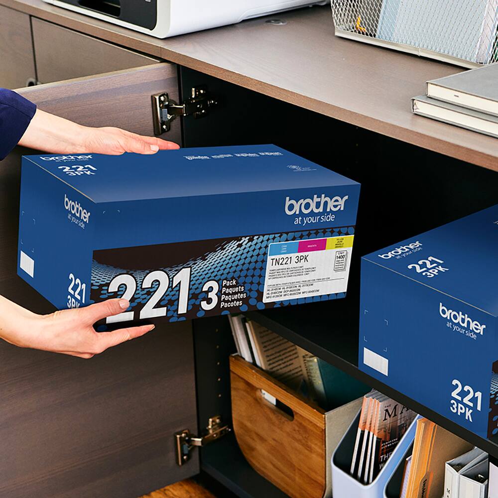 The text on the image is in Spanish, so I cannot provide a corrected version in English. However, I can provide a general description of the text:
The text is promoting a product called "Brother at your side," which is a 221 3PK pack. The pack contains 221 3V ink cartridges, and it is available in different languages. The image shows a person holding a box of this product, and there are other boxes of the same product in the background.