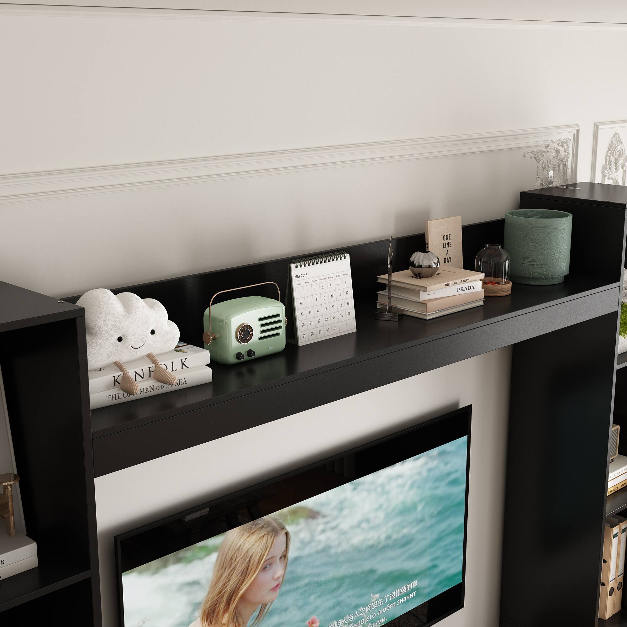The image features a shelf with a television on it. The television is on and displaying a picture of a woman. There are also several books on the shelf, as well as a teddy bear and a clock. Additionally, there is a vase and a cup placed on the shelf. The shelf is located in front of a wall, and there is a calendar on the wall as well.