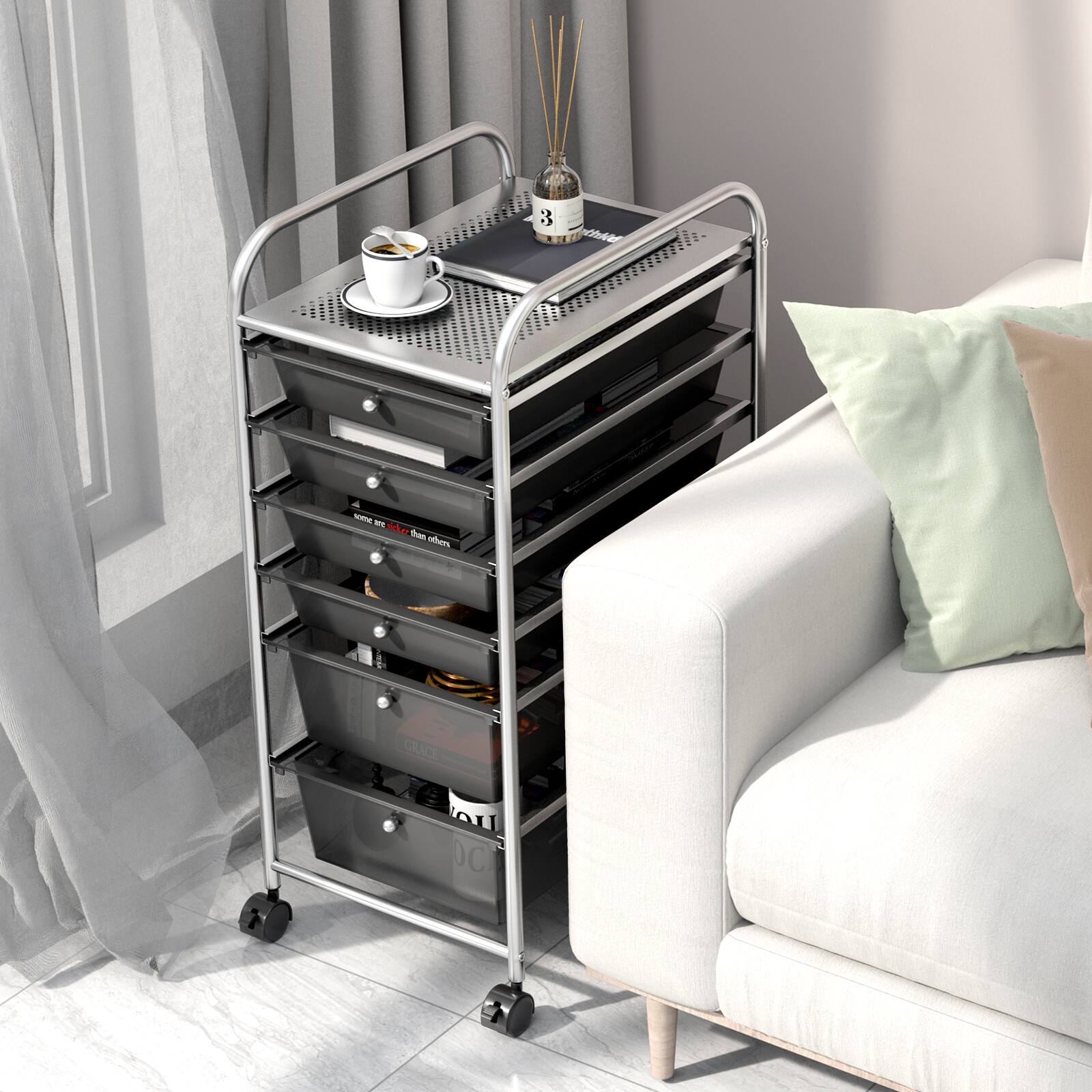 The image shows a small cart with a tray on top of it, placed next to a white couch. The tray has a cup of coffee and a candle on it. The cart is filled with various items, including books and a remote control. The couch is accompanied by a pillow, and the scene appears to be in a living room.