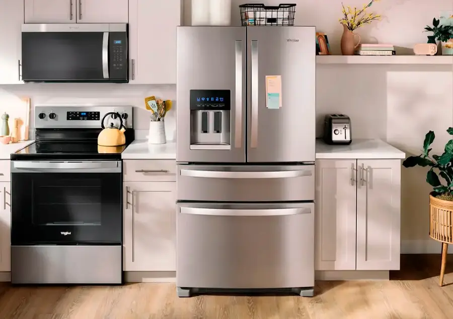 The image features a kitchen with a stainless steel refrigerator, a microwave, a stove, and a sink. The refrigerator is positioned between the stove and the sink, and there is a microwave above the stove. A potted plant is placed on the counter, and a vase is located on the kitchen counter as well. Additionally, there is a book on the counter, and a bowl is placed nearby. The kitchen is well-equipped and organized, providing a comfortable space for cooking and meal preparation.