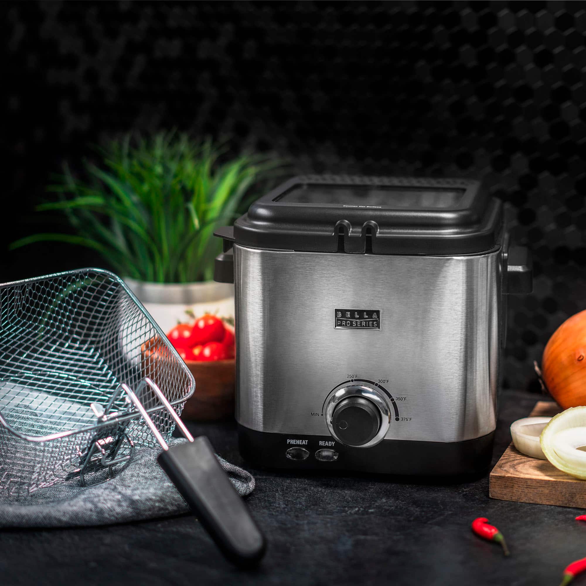 The image features a Bella 1 L & PRD Series 2504 S 201 d 2ST PREHEAT READY food processor on a counter. The food processor is surrounded by various ingredients, including a bowl of vegetables, a cutting board with onions, and a cutting board with peppers. The scene suggests that the food processor is being used to prepare a meal with these fresh ingredients.