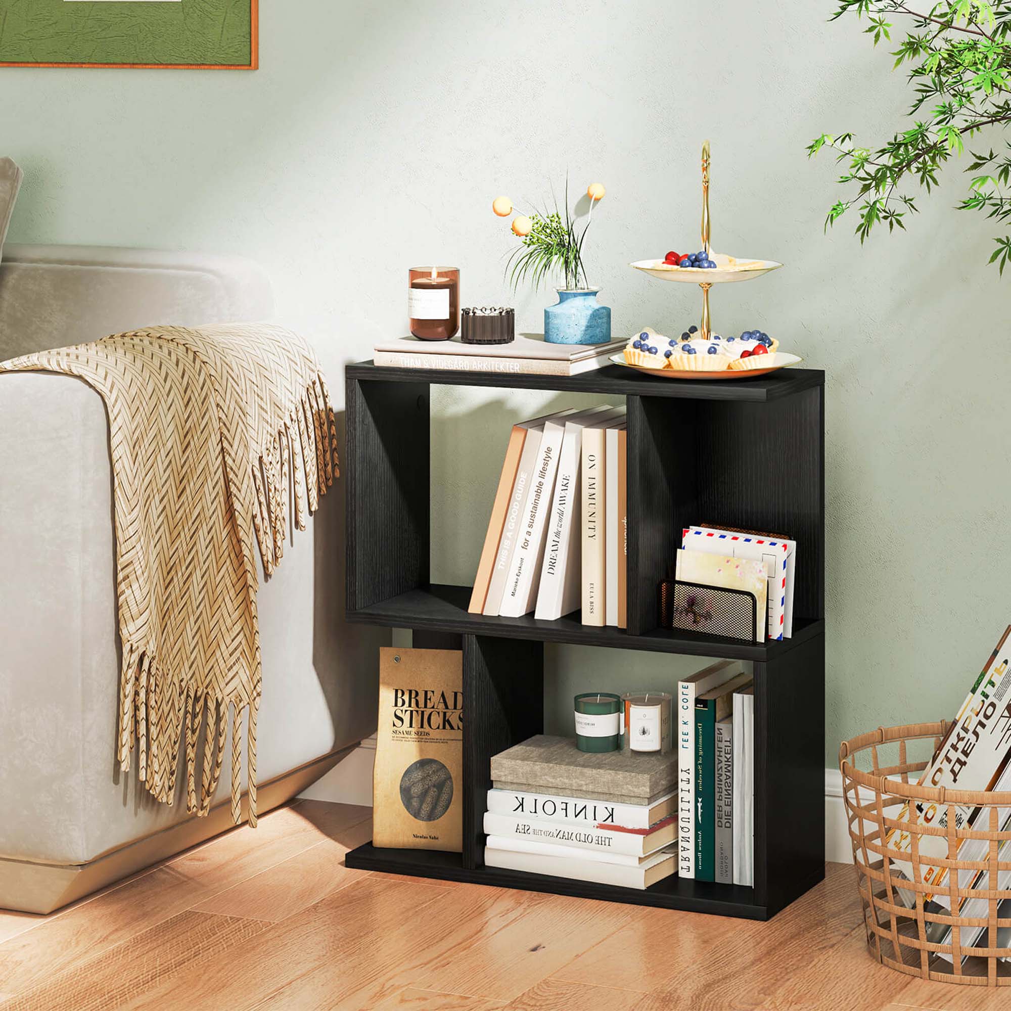 A bookshelf with a variety of books and items on it. The books are arranged in a way that they are easily accessible and visible. The bookshelf is placed on a wooden floor, and it is situated next to a couch. The books on the shelf include titles such as "Bread Sticks" and "Kinfold Sea Old." There are also some decorative items on the shelf, such as a vase and a potted plant.