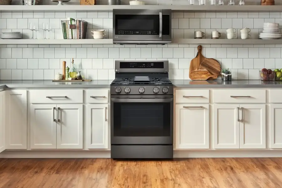 The image features a kitchen with a black oven and a white stove top. The oven is located in the middle of the kitchen, surrounded by white cabinets. The kitchen also has a sink and a microwave, both placed above the oven. Various items can be seen on the countertops, such as a bowl, a cup, and a bottle. Additionally, there are several books scattered around the kitchen, possibly cookbooks or recipe books.