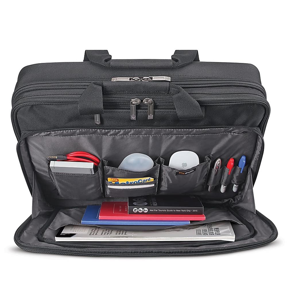 The image shows a black briefcase with a variety of items inside. The contents include a book, a laptop, a notebook, a pen, and a pair of scissors. The book is located on the left side of the briefcase, while the laptop is positioned in the middle. The notebook is placed on the right side, and the pen and scissors are located towards the bottom of the briefcase. The briefcase is open, revealing the assortment of items inside.