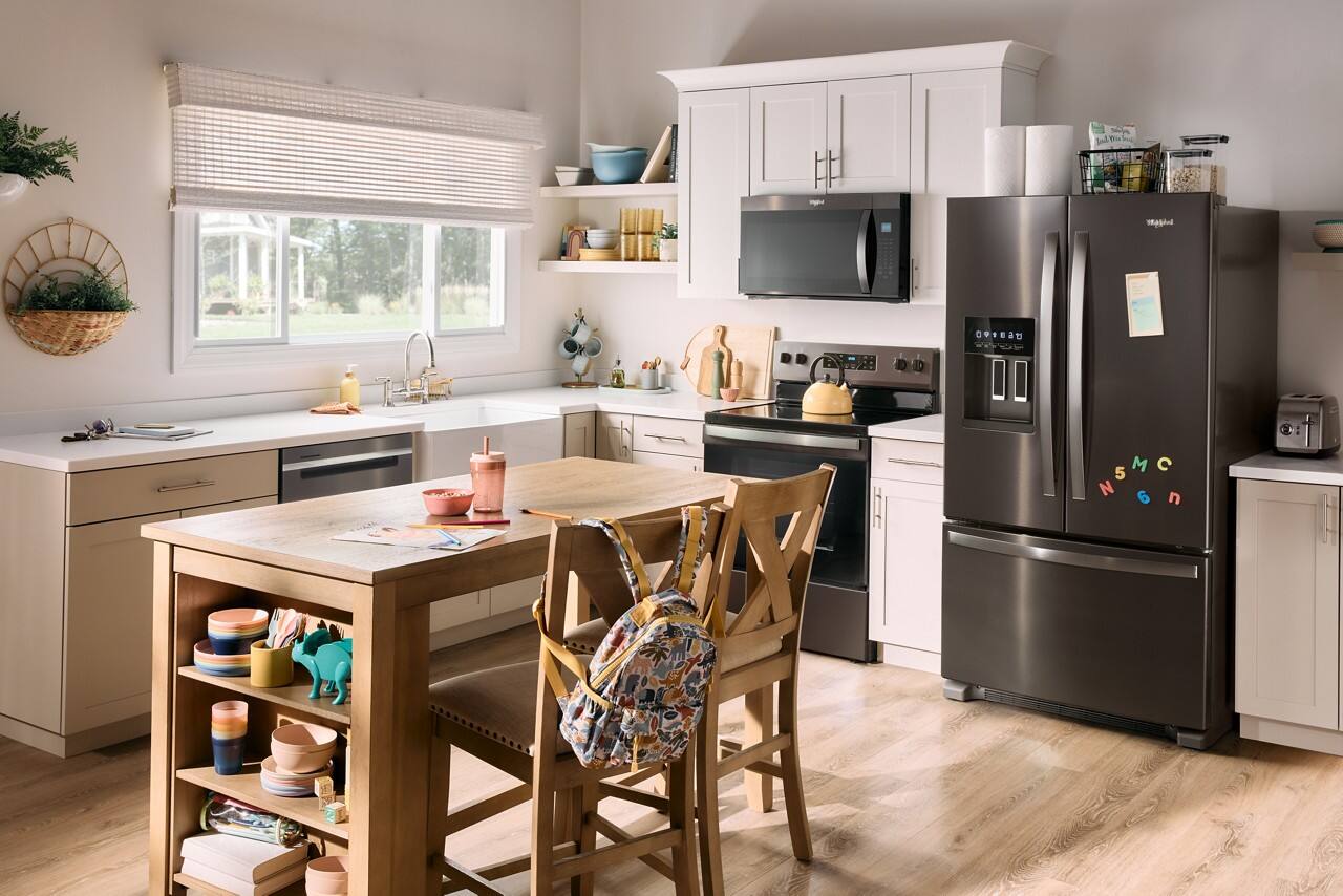 The image shows a kitchen with a large refrigerator, a sink, a dining table, and chairs. The kitchen is clean and well-organized, with a variety of items on the countertops. There are several bowls, cups, and bottles placed around the kitchen, as well as a potted plant and a vase. The dining table is surrounded by chairs, and there is a book on the table. The kitchen is well-equipped with appliances such as a microwave and an oven, making it a functional and inviting space.
