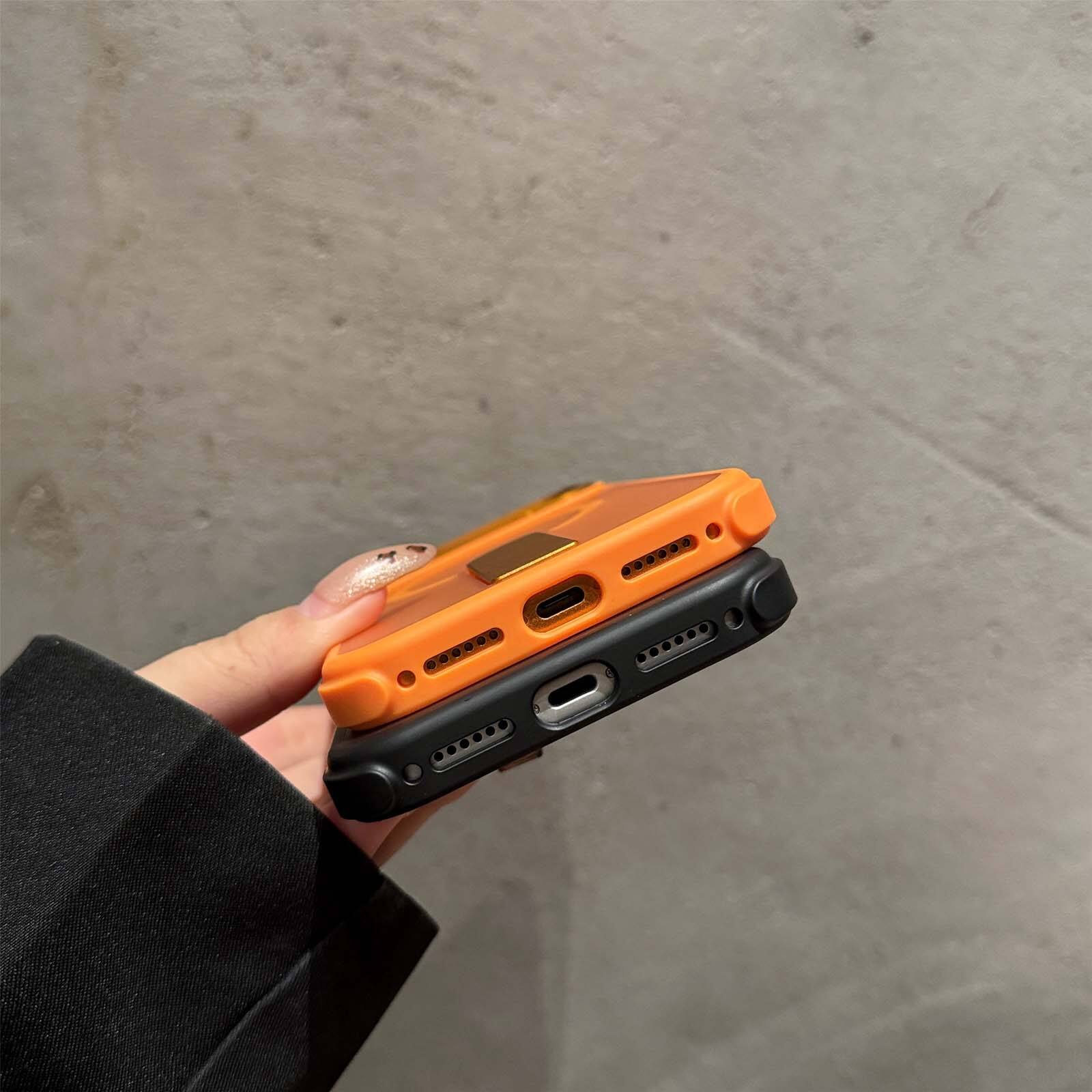 The image shows a close-up of a person's hand holding two smartphones with orange and black cases. The phones have visible ports and buttons on the side.