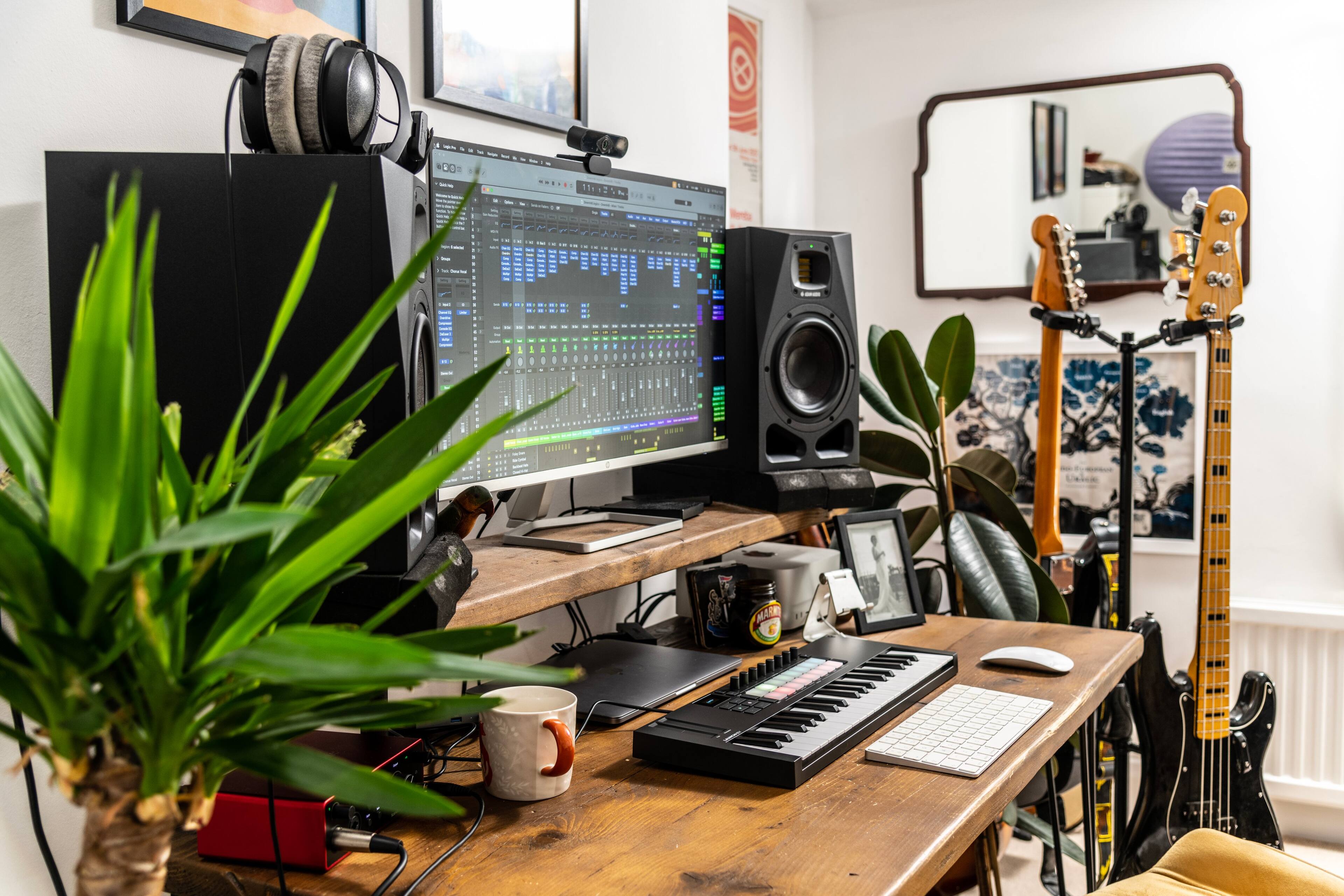 The image shows a home office with a desk and a computer setup. On the desk, there is a keyboard, a mouse, and a cup. A computer monitor is also present in the room. In addition to the computer equipment, there are two potted plants, one on the left side of the desk and the other on the right side. A TV is mounted on the wall above the desk. A pair of scissors can be seen on the desk, along with a cell phone. A chair is positioned in front of the desk, and a remote control is placed nearby.