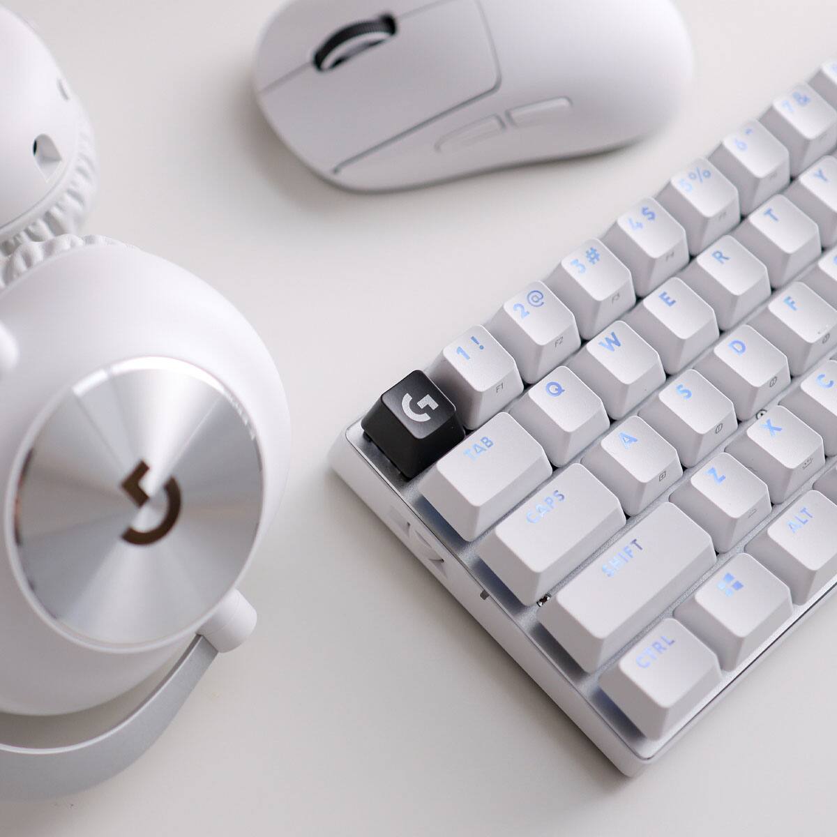 The image features a white keyboard with a black G key in the middle. The keyboard is placed on a white table, and a computer mouse is positioned nearby. The keyboard has a unique design with a combination of white and blue keys.