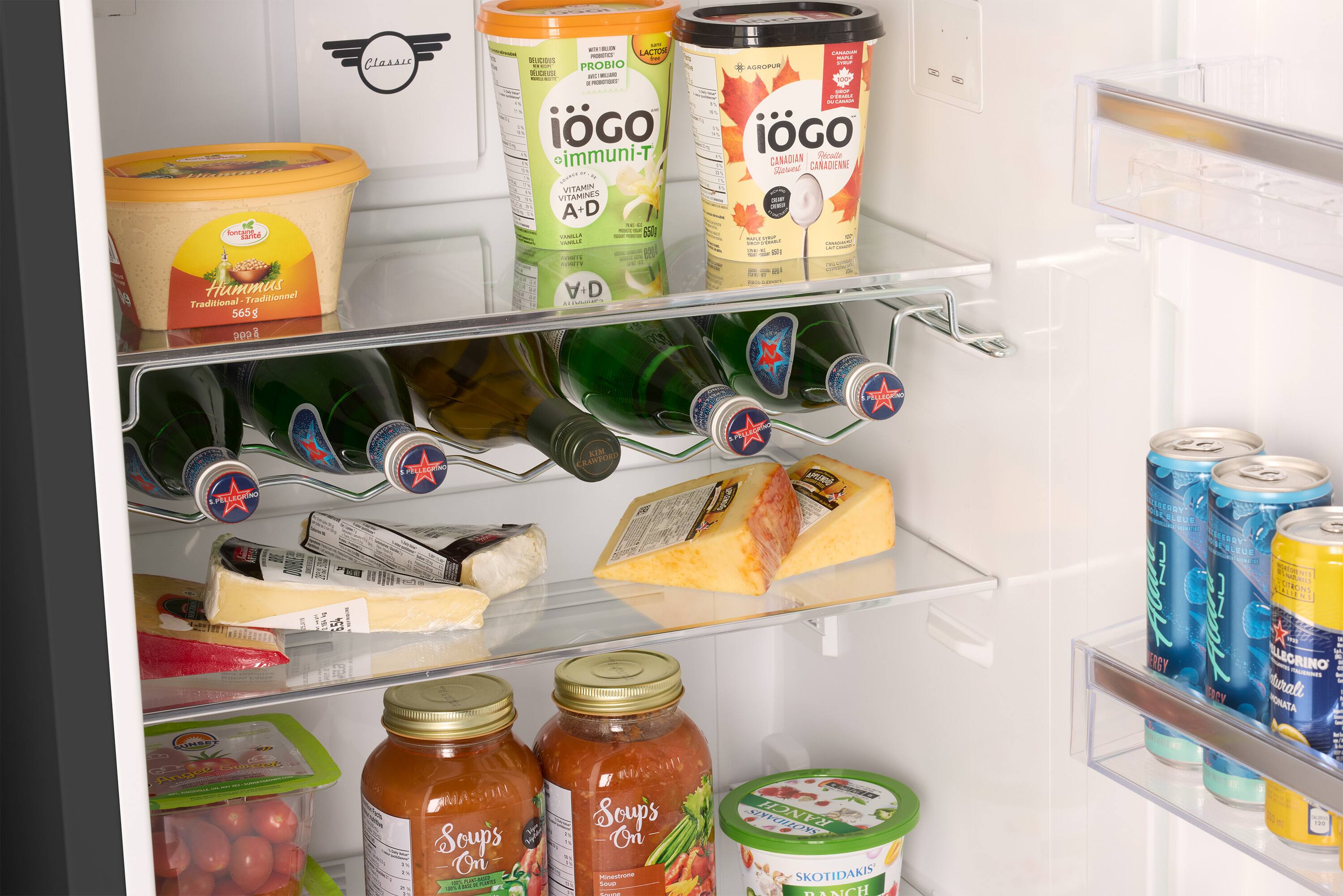The refrigerator is filled with various food items, including a carton of eggs, a bottle of wine, and a container of hummus. There are also several bottles of juice and milk, as well as a few cans of soda. The refrigerator is well-stocked and ready for use.