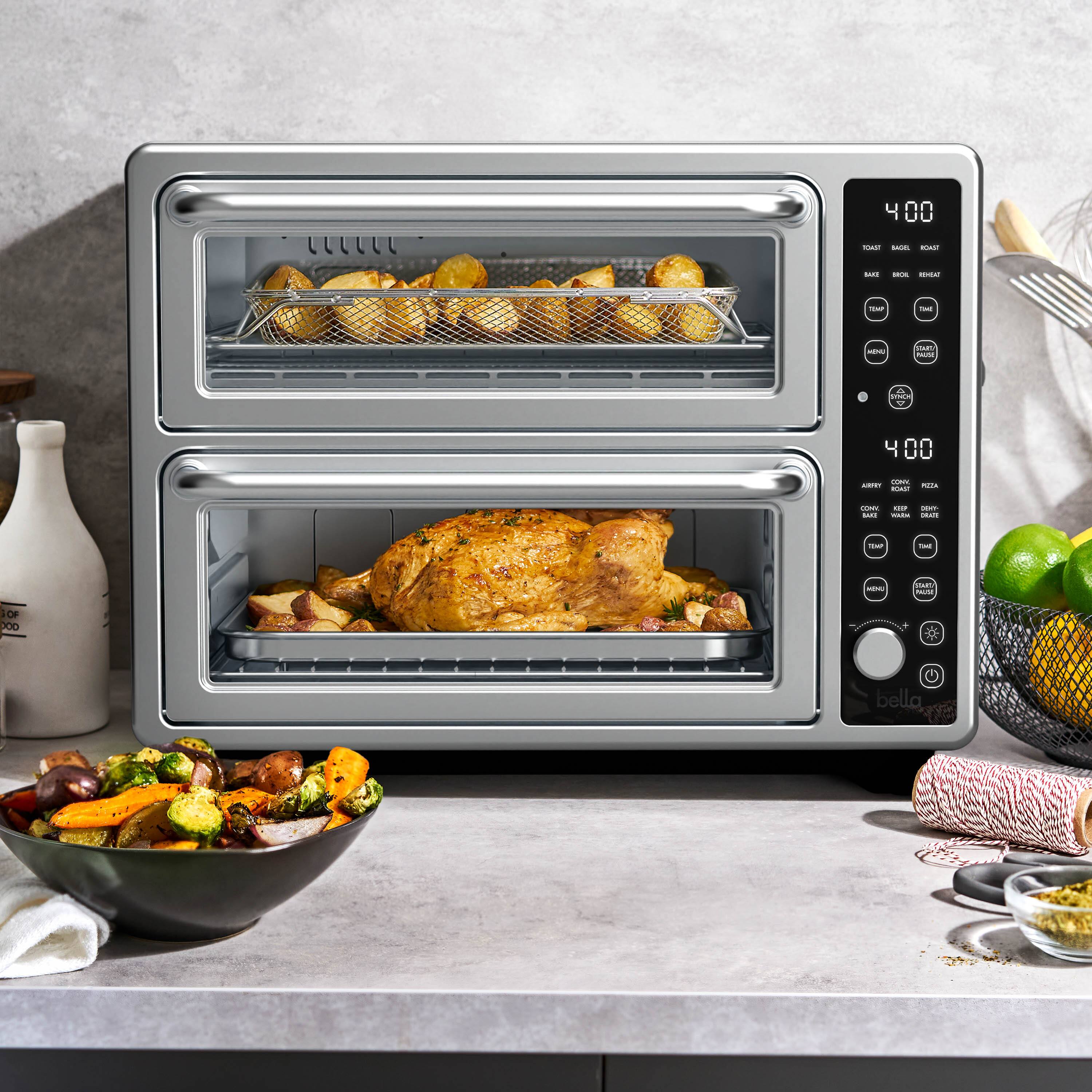 The image features a kitchen counter with a toaster oven and a bowl of food. The toaster oven is open, revealing a tray of food inside. The bowl of food is placed next to the toaster oven, and there are also some carrots visible in the scene. Additionally, there is a fork and a knife nearby, likely used for serving the food. The image also contains a clock, which is mounted on the wall above the counter.