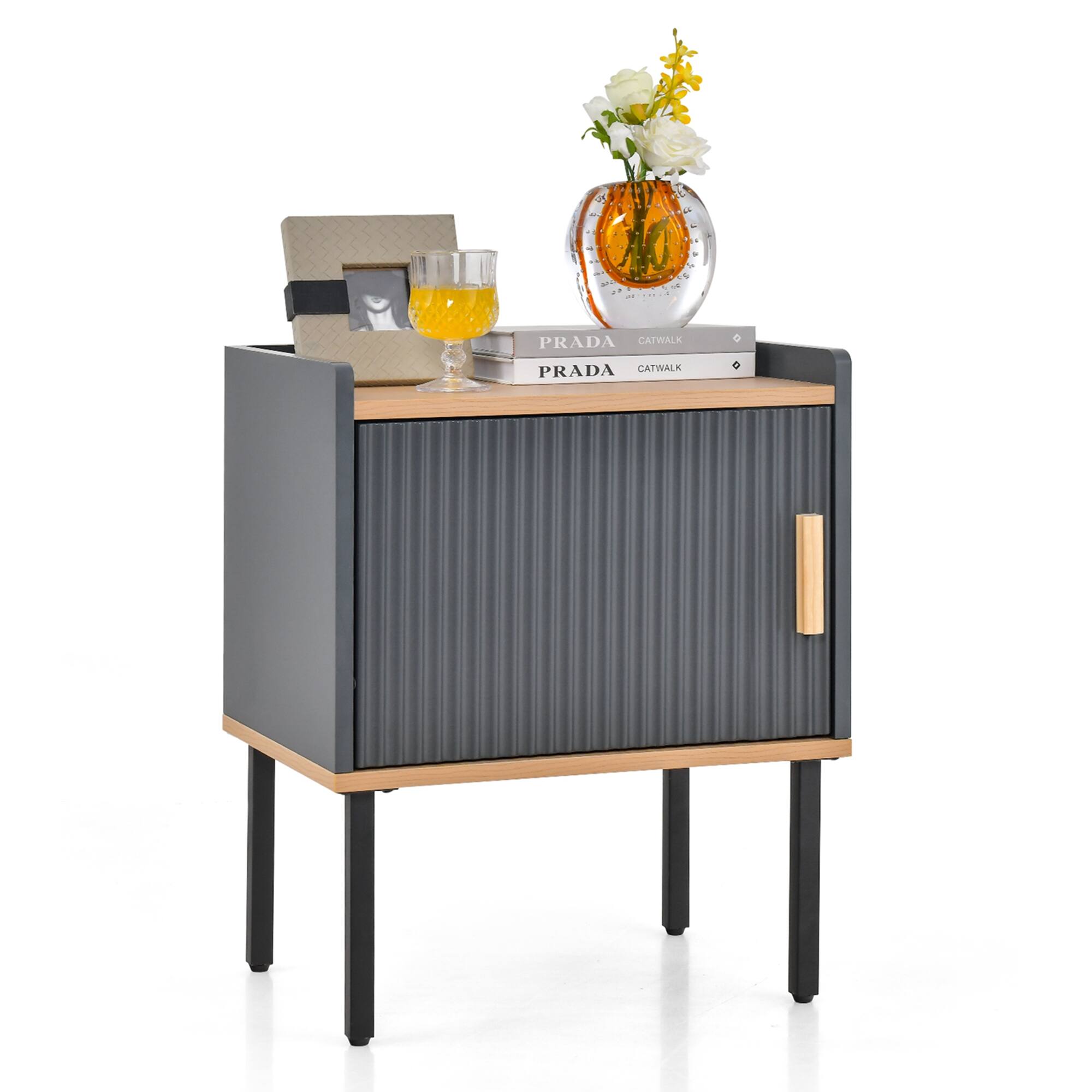 The image features a small table with a glass of orange juice on it. There is also a vase with flowers and a book placed on the table. The table is made of wood and has a metal frame.