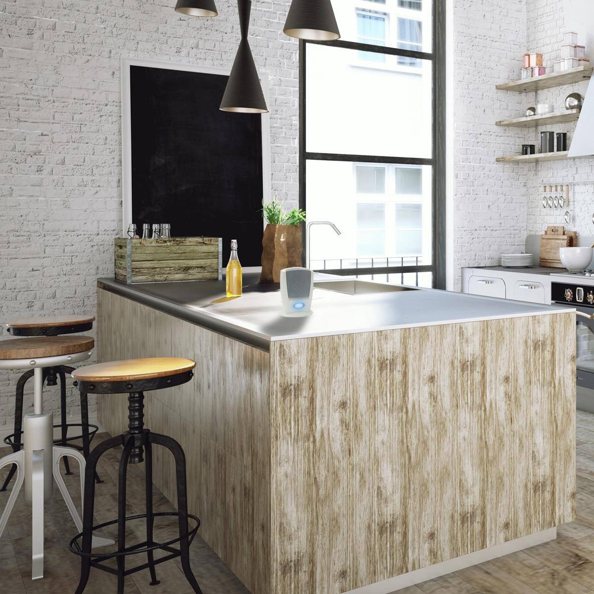 The image shows a modern kitchen with a central island. The island has a light wood finish and a metallic countertop. There are two bar stools with round seats and black metal legs. The kitchen features white brick walls, a large window, and shelves with various kitchen items. A bottle of yellow liquid is placed on the island.