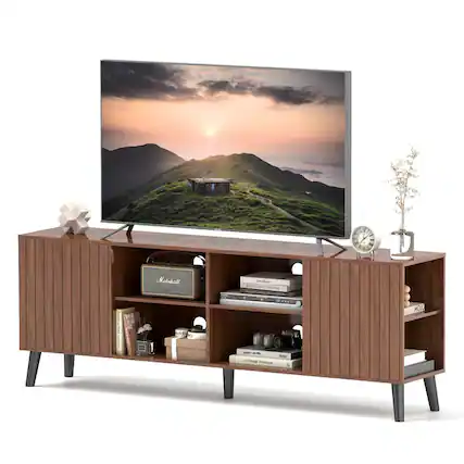 The image features a large flat-screen TV sitting on top of a wooden entertainment center. The TV is displaying a beautiful sunset scene. The entertainment center has a clock on it, and there are several books placed nearby. Additionally, there is a vase and a potted plant in the scene, adding to the overall aesthetic of the space.