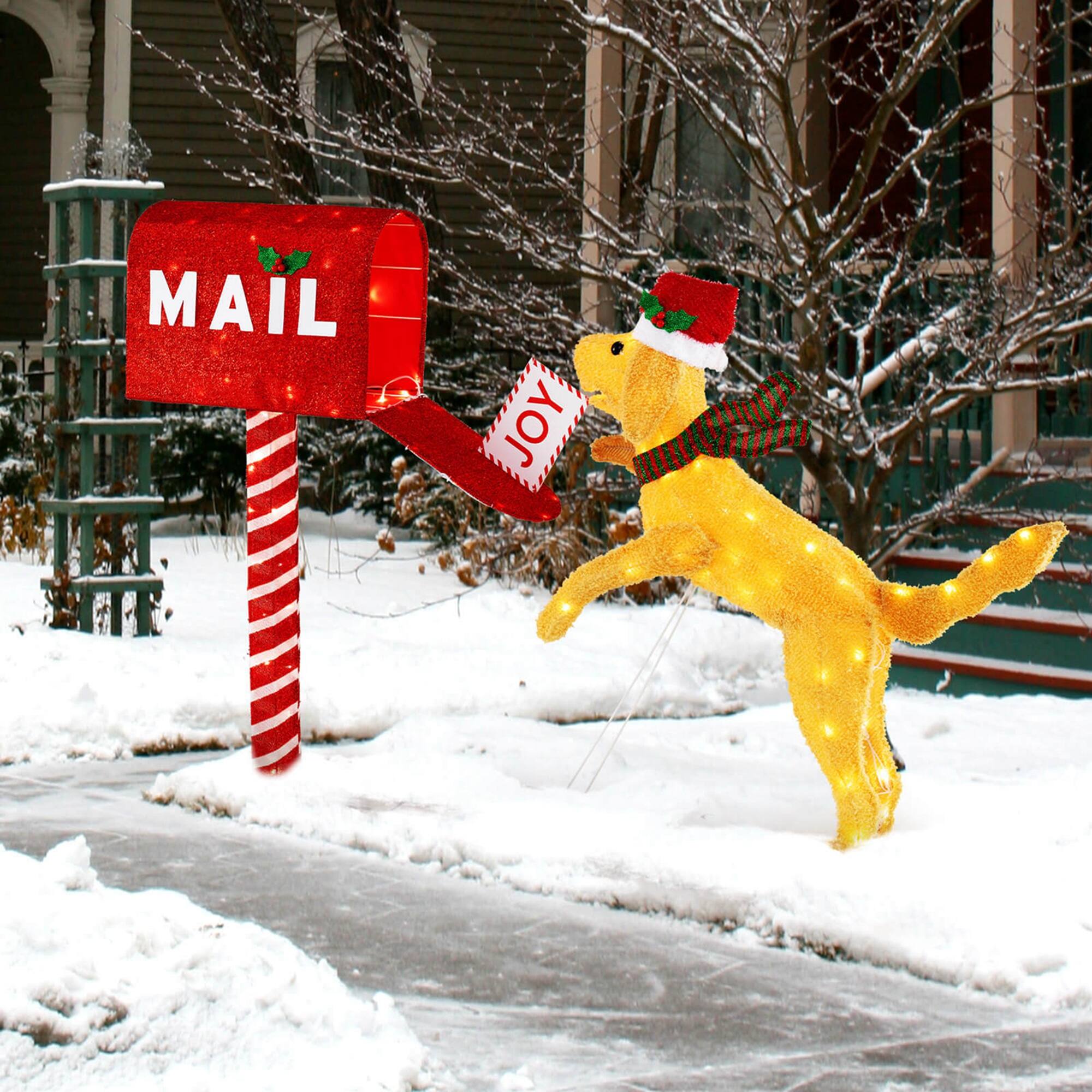 The image shows a festive scene with a red mailbox labeled "MAIL" and a dog wearing a Santa hat and scarf. The dog is leaping to catch a letter that is being ejected from the mailbox. The setting is snowy, with trees and a building in the background.