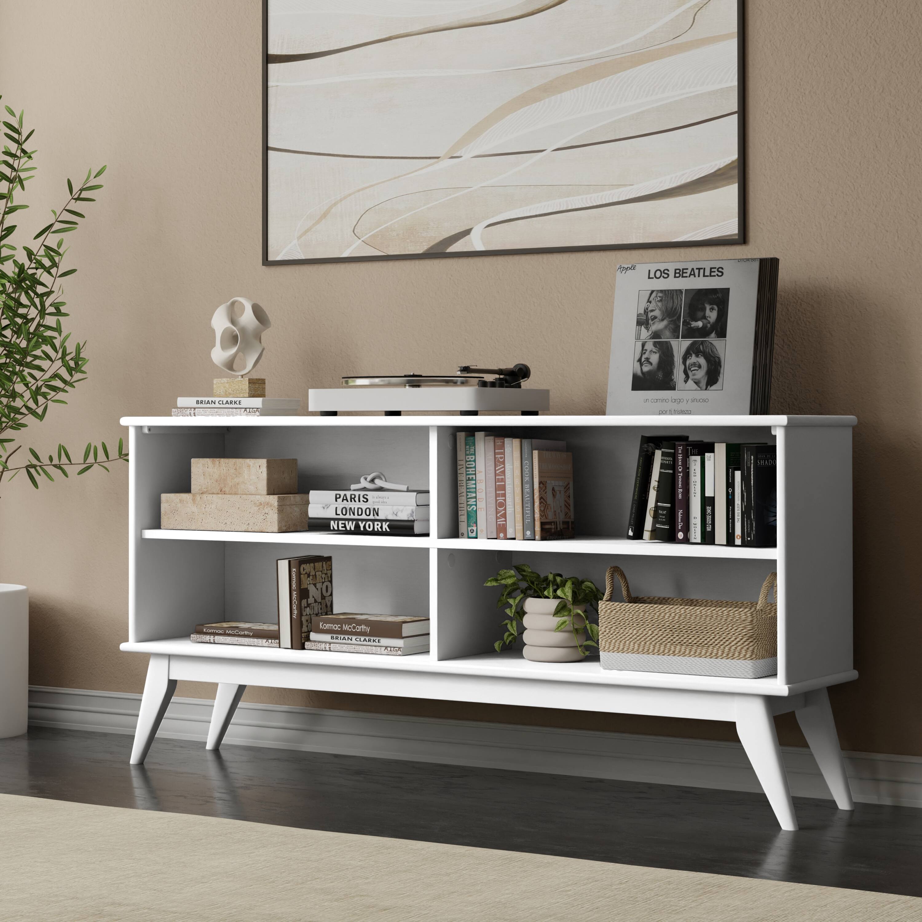 Sure, here is the corrected and grouped text from the image:

---

**Top Shelf:**
- LOS BEATLES
- Apple
- "in the city" vinyl
- "Sgt. Pepper's Lonely Hearts Club Band" vinyl

**Middle Shelf:**
- PARIS
- LONDON
- NEW YORK

**Bottom Shelf:**
- BRIAN CLARKE
- KOMIKA McCLARKE
- KOMIKA McCLARKE
- BRIAN CLARKE

**Books:**
- (Various titles visible, but not fully legible)

**Other Items:**
- A plant
- A wicker basket

---