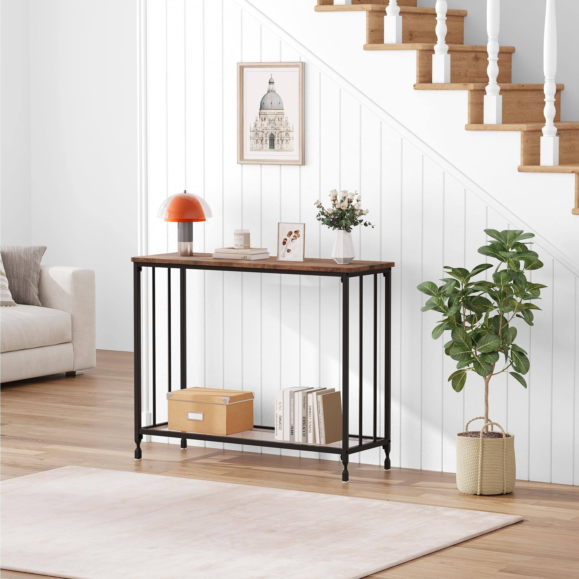 1. NATO: SES7Ard

2. The image shows a well-organized living space with a focus on a console table. The table has a lamp with an orange shade, a framed picture, a small vase with flowers, and a few books. Below the table, there is a wooden box and more books. To the right, there is a potted plant in a woven basket. The background features a staircase with white railings and a framed picture of a domed building on the wall.