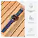 The image shows a Garmin watch with a blue band sitting on a wooden surface. The watch has a built-in flashlight and is equipped with chartplotter voice commands. The watch also has a regatta timer and is designed to be used with Bluetooth technology.
