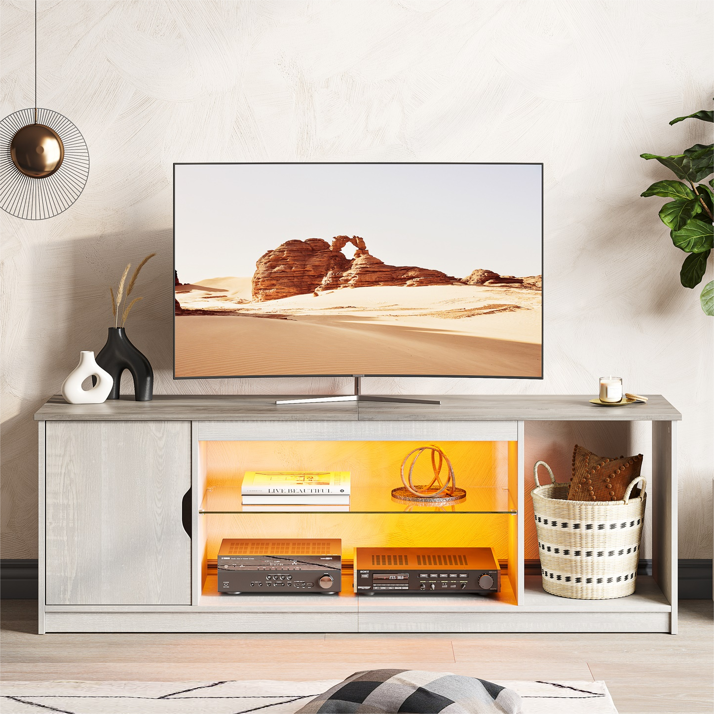 The image features a flat screen TV sitting on top of a wooden stand. The TV is displaying a picture of a desert landscape, and there are several books placed on the stand. Additionally, there is a potted plant located to the right of the TV, and a vase can be seen on the left side of the stand. The overall scene creates a cozy and inviting atmosphere in the living space.