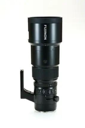 The image features a large black lens, which is a Fujinon lens. The lens is sitting on a white background, making it stand out prominently. The lens is designed for use with a camera, and it is likely to be a high-quality optic for capturing images with exceptional clarity and detail.