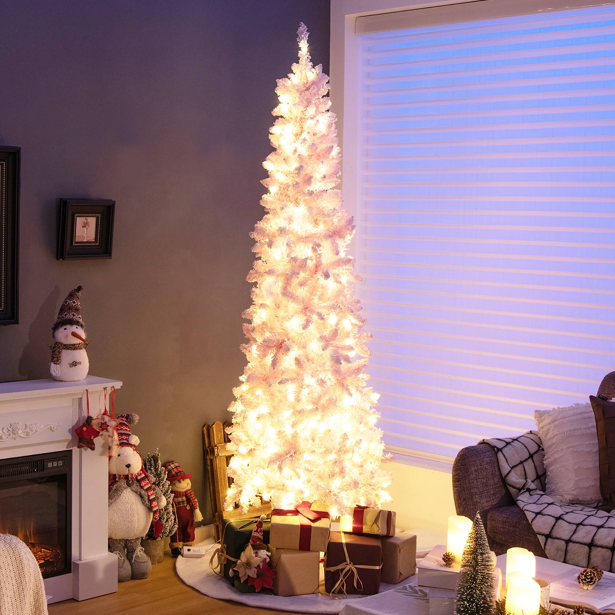 The image shows a beautifully decorated living room with a lit Christmas tree in the corner. The room is furnished with a couch, a chair, and a fireplace, creating a cozy atmosphere. The Christmas tree is adorned with presents, and there are several teddy bears scattered around the room, adding a playful touch to the festive decorations. The room also features a window, which allows natural light to enter and enhances the overall ambiance.
