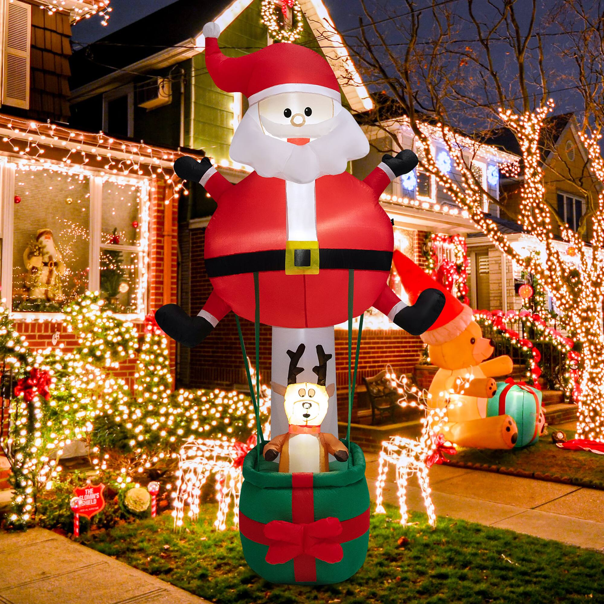 The text "DE p's PCELD" is not relevant to the image. It seems to be an unrelated or incorrect description. The image features a large inflatable Santa Claus and reindeer decoration in front of a house, along with other Christmas decorations.