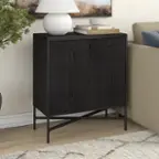 The image shows a small black dresser in a living room. The dresser is placed on a hardwood floor and has a lamp on top of it. There are also several books on the dresser, adding to the room's cozy atmosphere. The dresser is situated next to a couch, creating a comfortable and functional space for relaxation and reading.