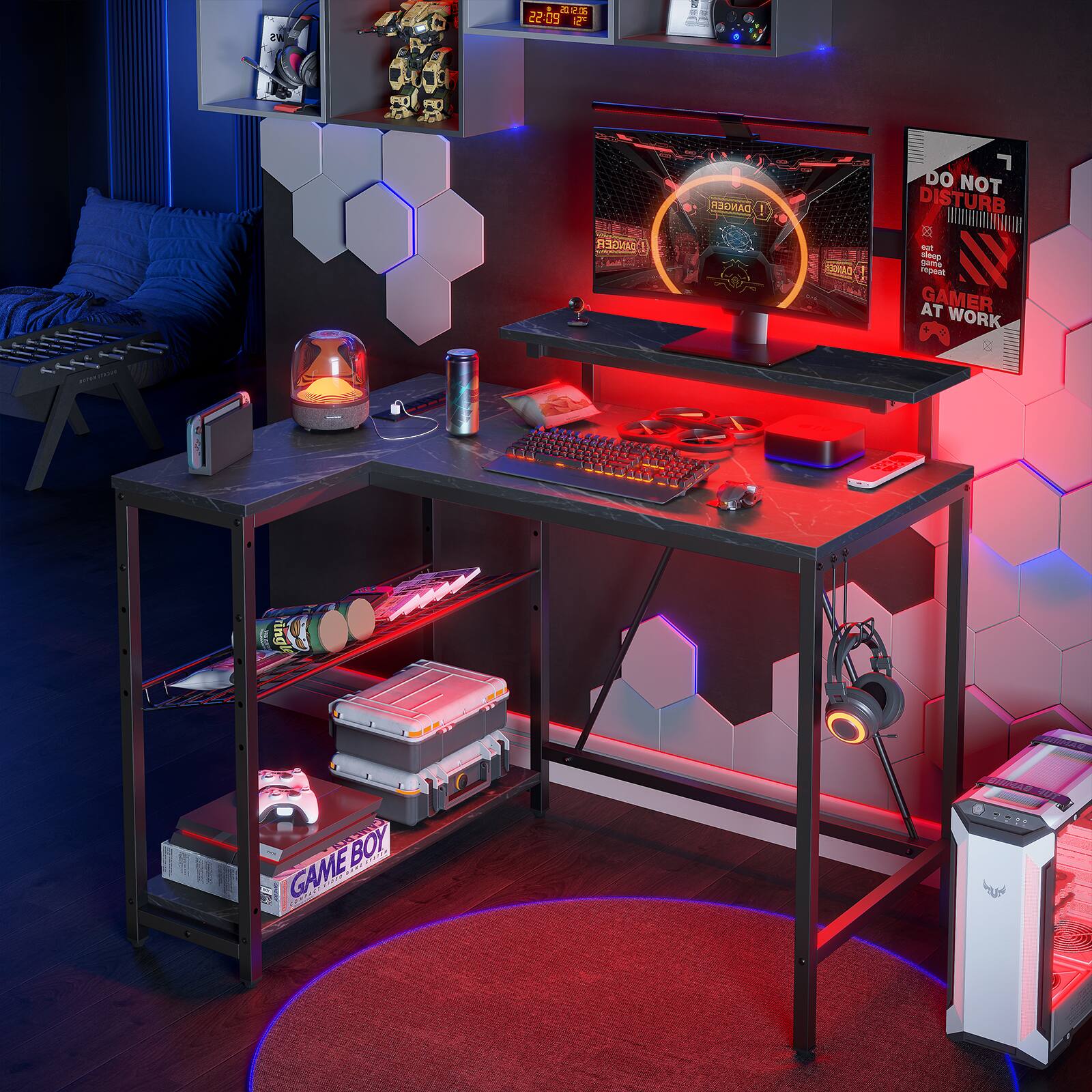 The image features a computer desk with a monitor, keyboard, and mouse. The desk is illuminated by red lights, creating a gaming atmosphere. There is a Game Boy on the desk, as well as a laptop and a cell phone. A couch can be seen in the background, and a book is placed nearby. The image also includes a TV, which is mounted on the wall above the desk.