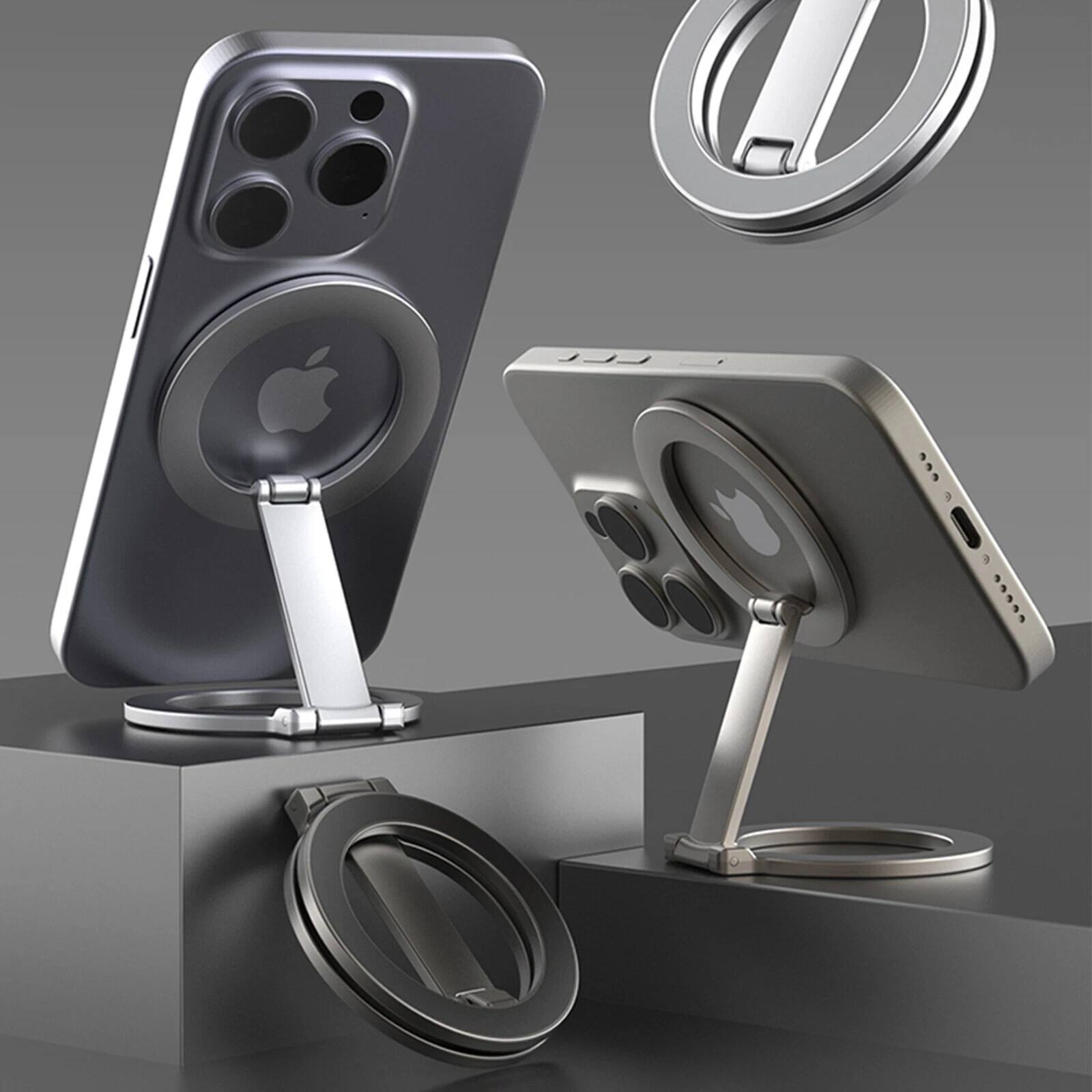 The image shows a sleek, modern smartphone stand designed to hold a smartphone in a vertical position. The stand features a minimalist, metallic design with a circular base and a sturdy arm that holds the phone securely. The phone itself is a high-end model with a prominent Apple logo on the back, indicating it's an iPhone. The stand is positioned on a reflective surface, and there are additional stands visible in the background, suggesting it's part of a product display or advertisement.